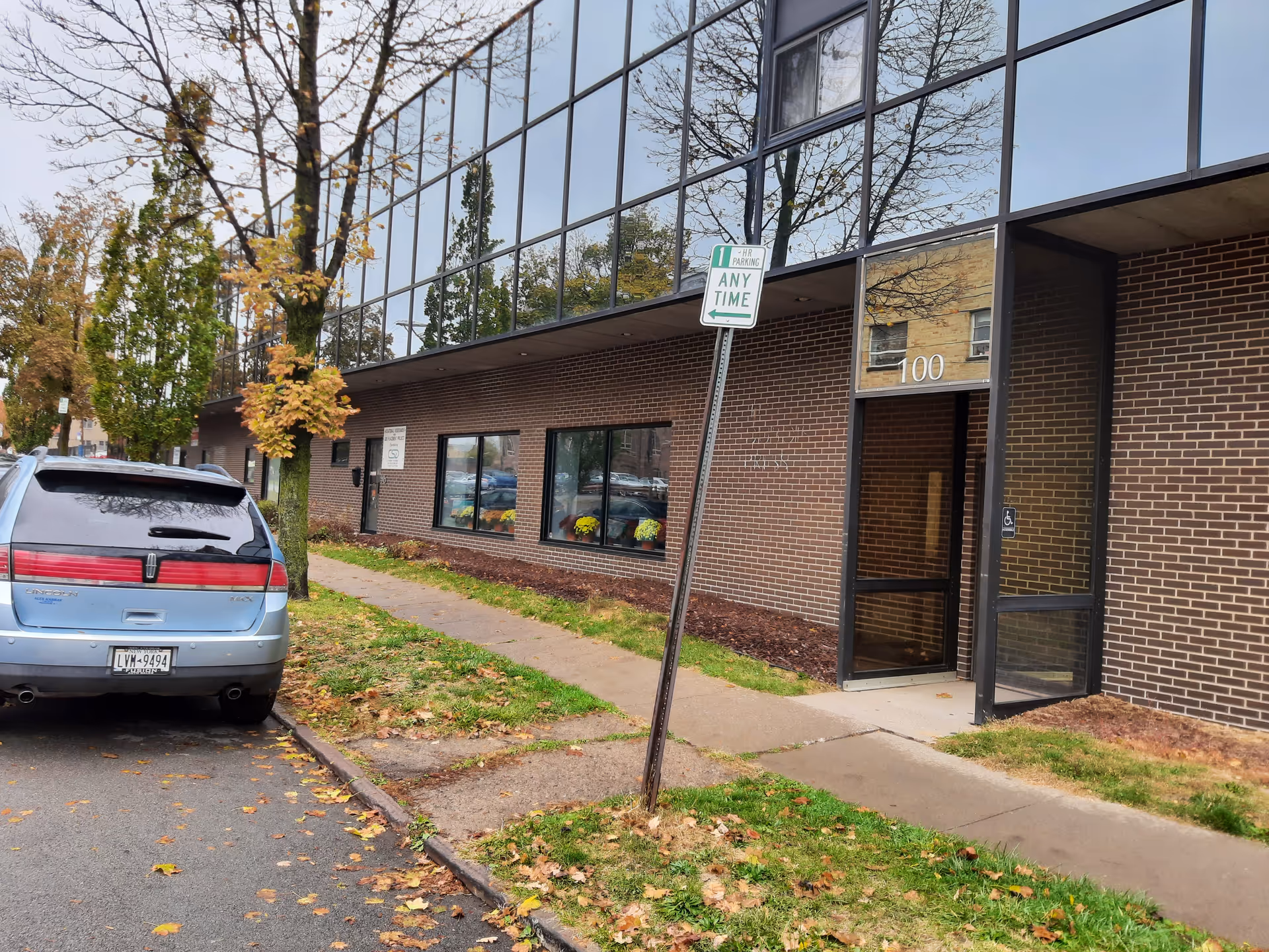 Exterior view of a brick building with glass windows, a doorway, and a parked blue minivan.