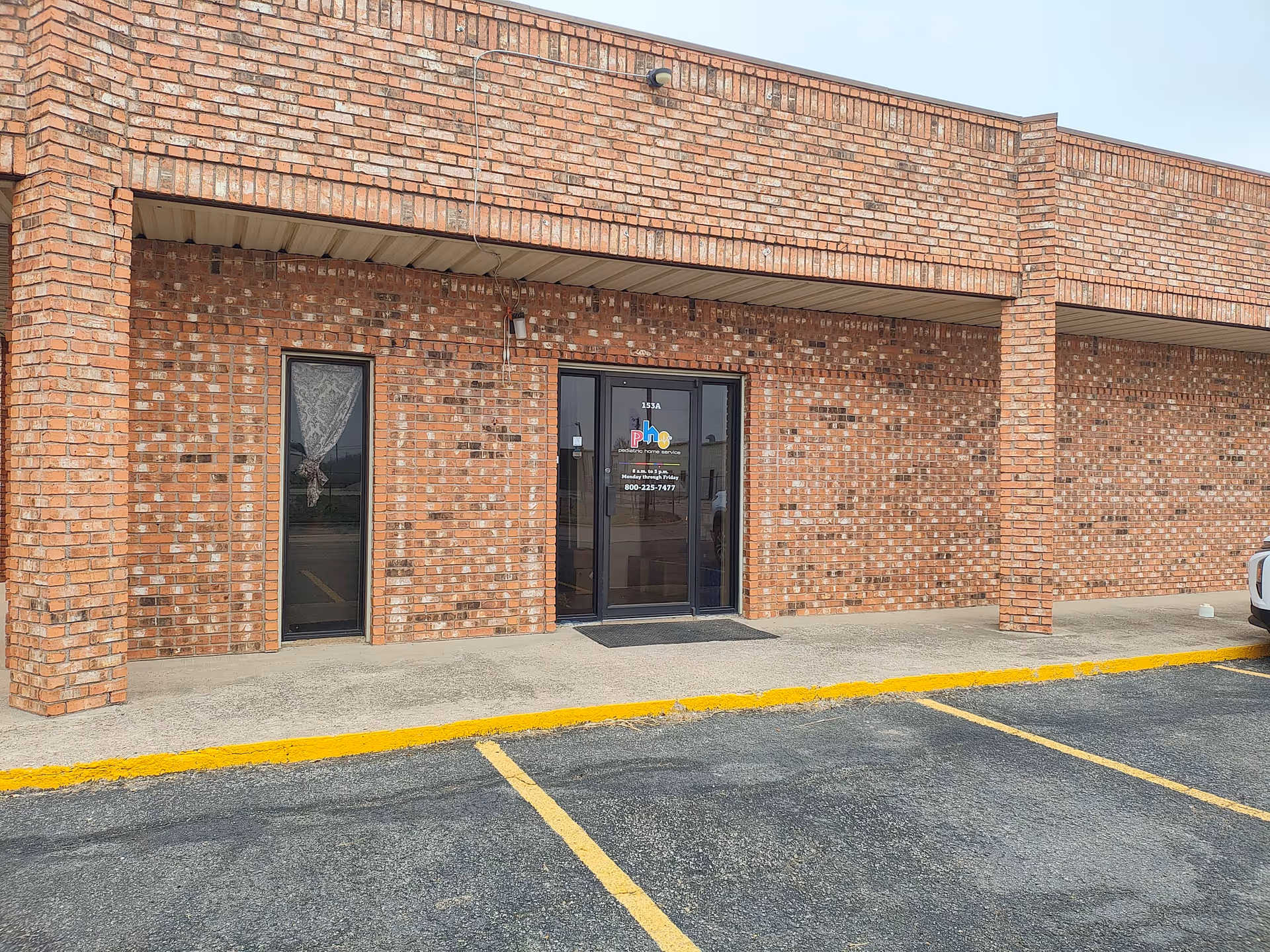 Brick facility exterior with glass entrance doors and a parking lot.