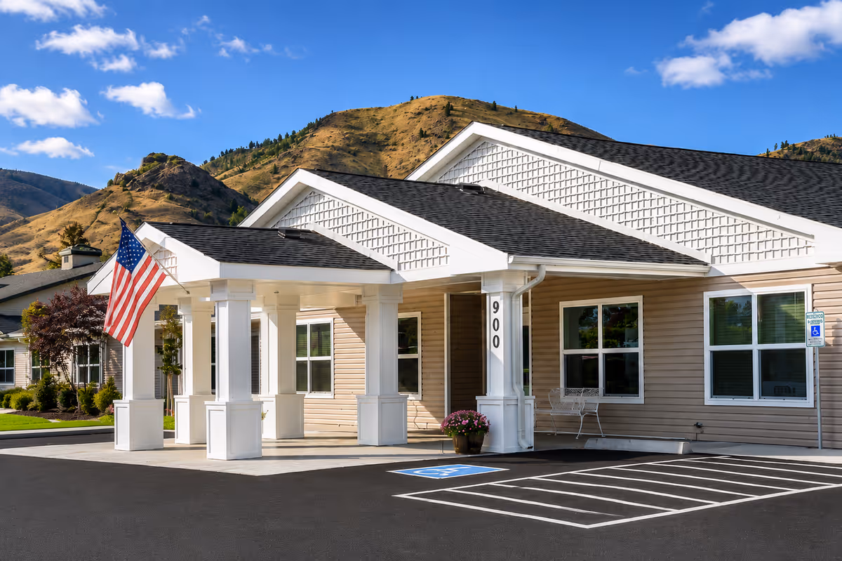 Exterior view of RiverWest senior living facility entrance with flag and parking.