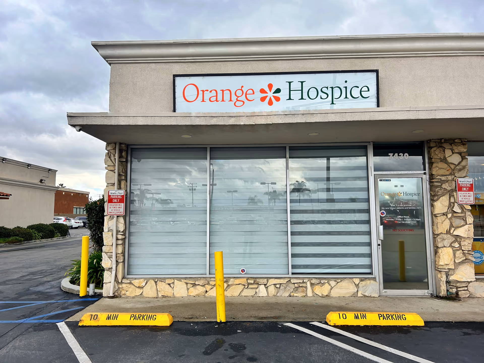Front view of Orange Hospice storefront with large windows, stone facade, and parking.