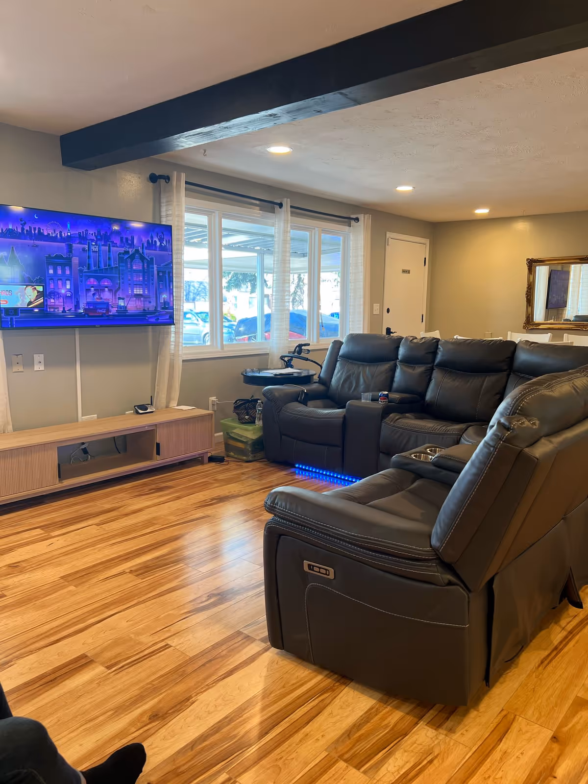 Cozy living room with leather recliners, TV, wooden floor, and large windows.
