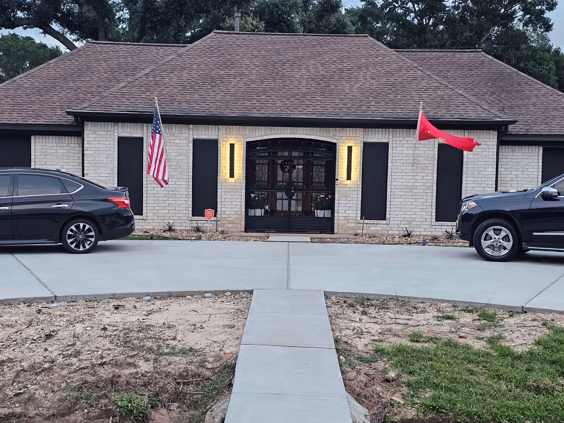 Front view of a single-story brick senior living home with flags and parked cars.