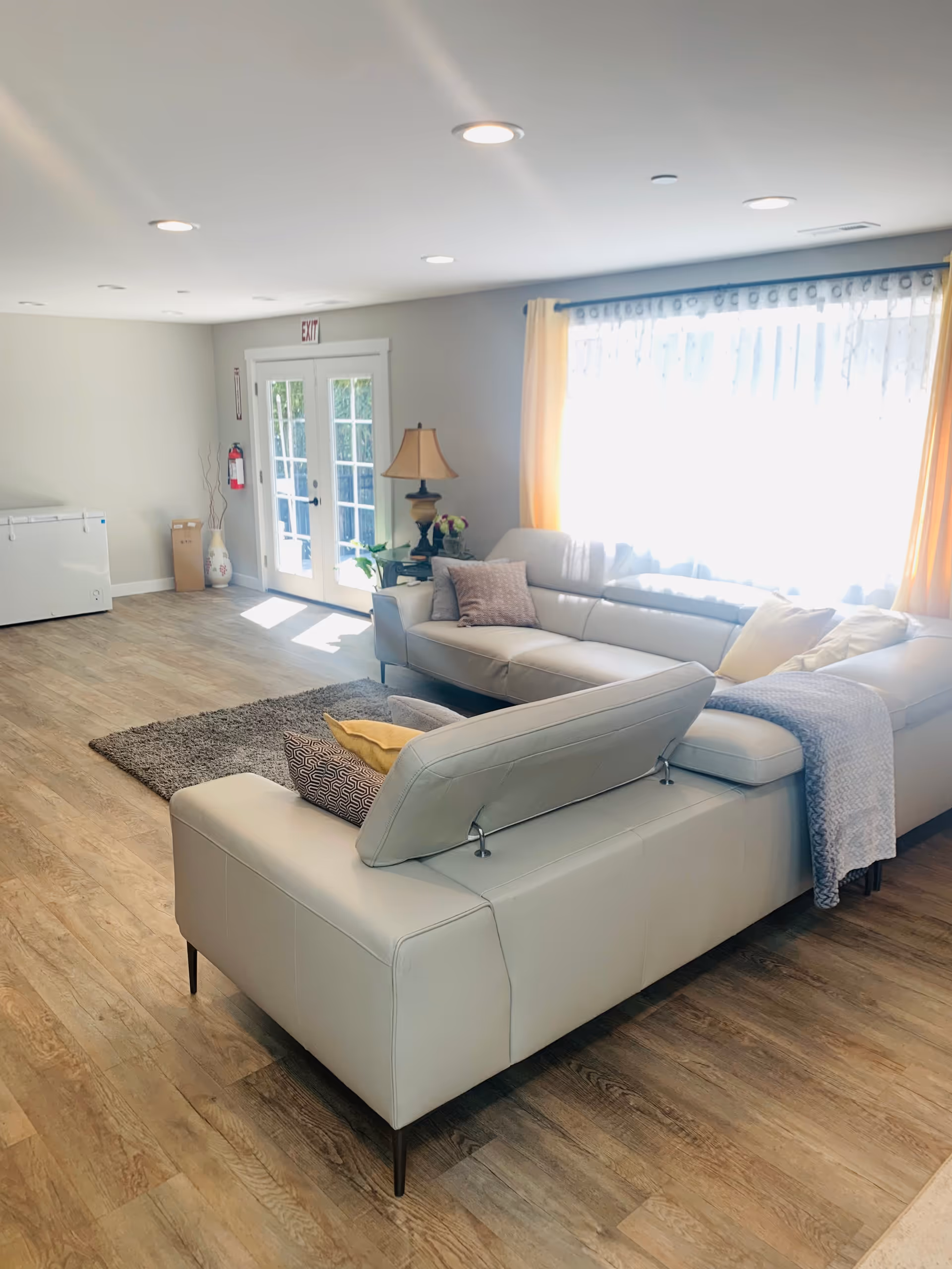 Bright, modern living room with white sofas, a rug, and large window curtains.