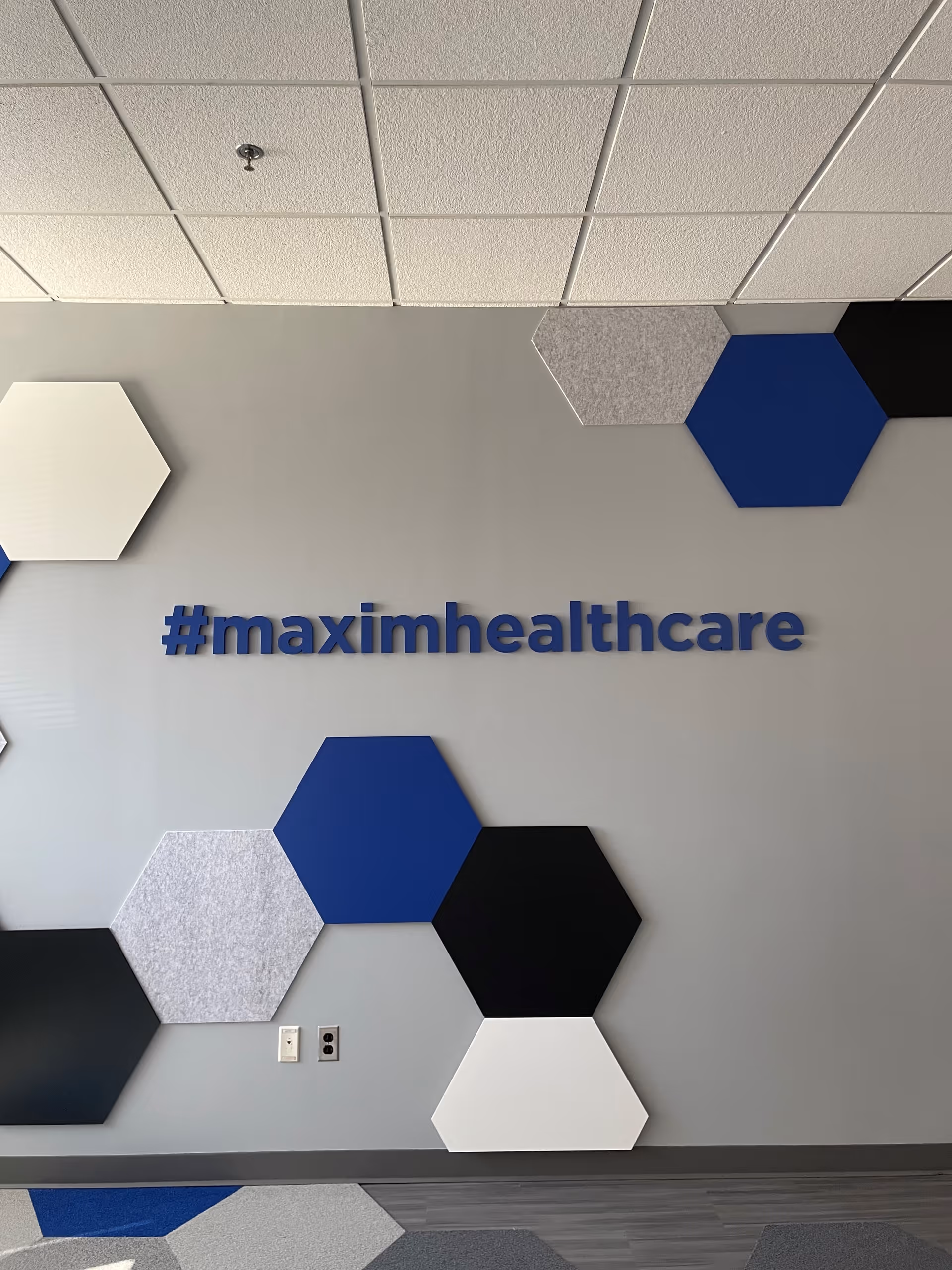 Interior wall featuring geometric hexagon decor and '#maximhealthcare' sign.