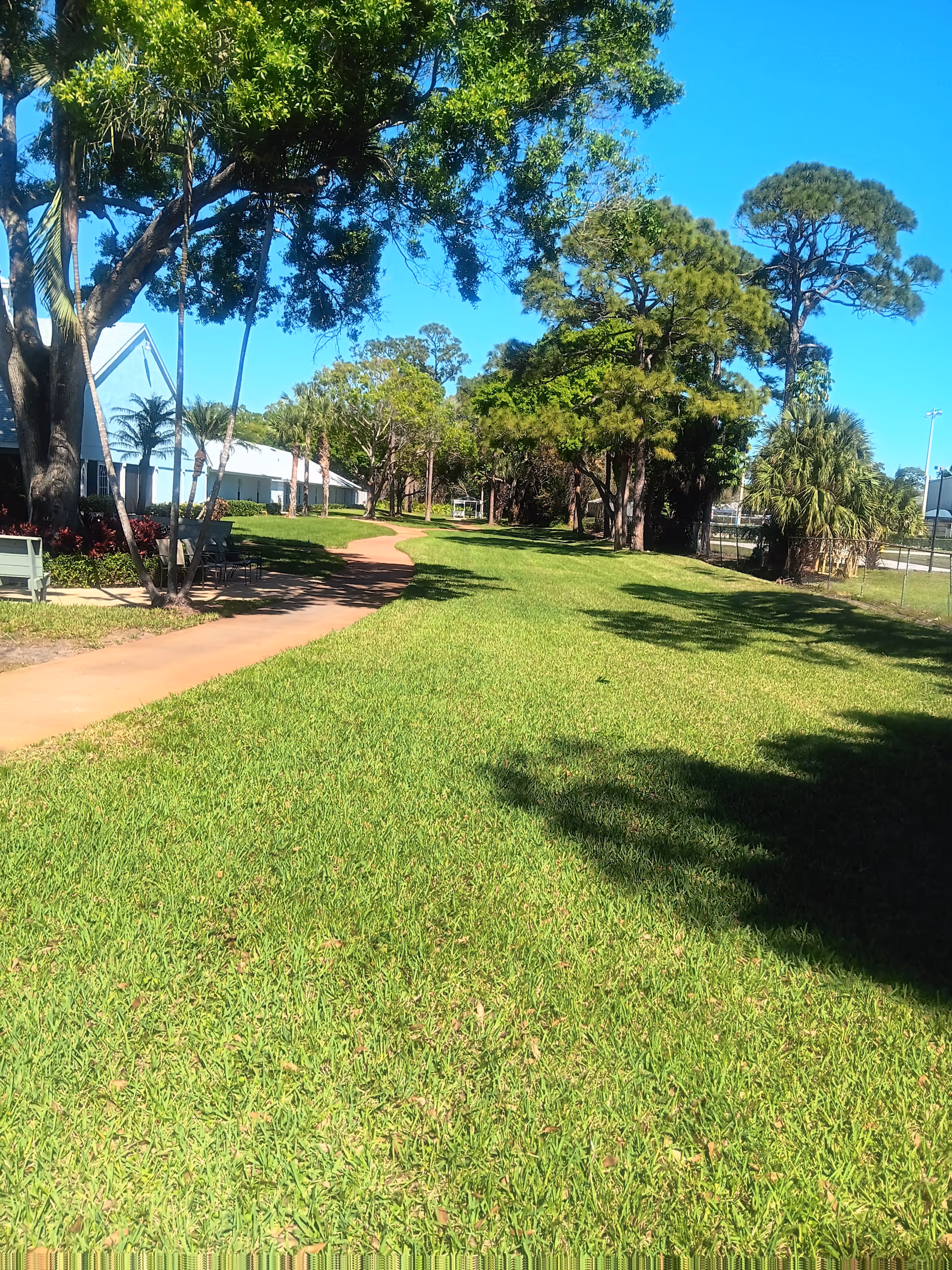Sunny outdoor lawn beside a senior living facility with a winding path and benches.