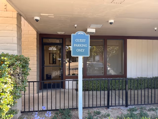 Entrance to senior facility with guest parking sign, glass doors, and railing.