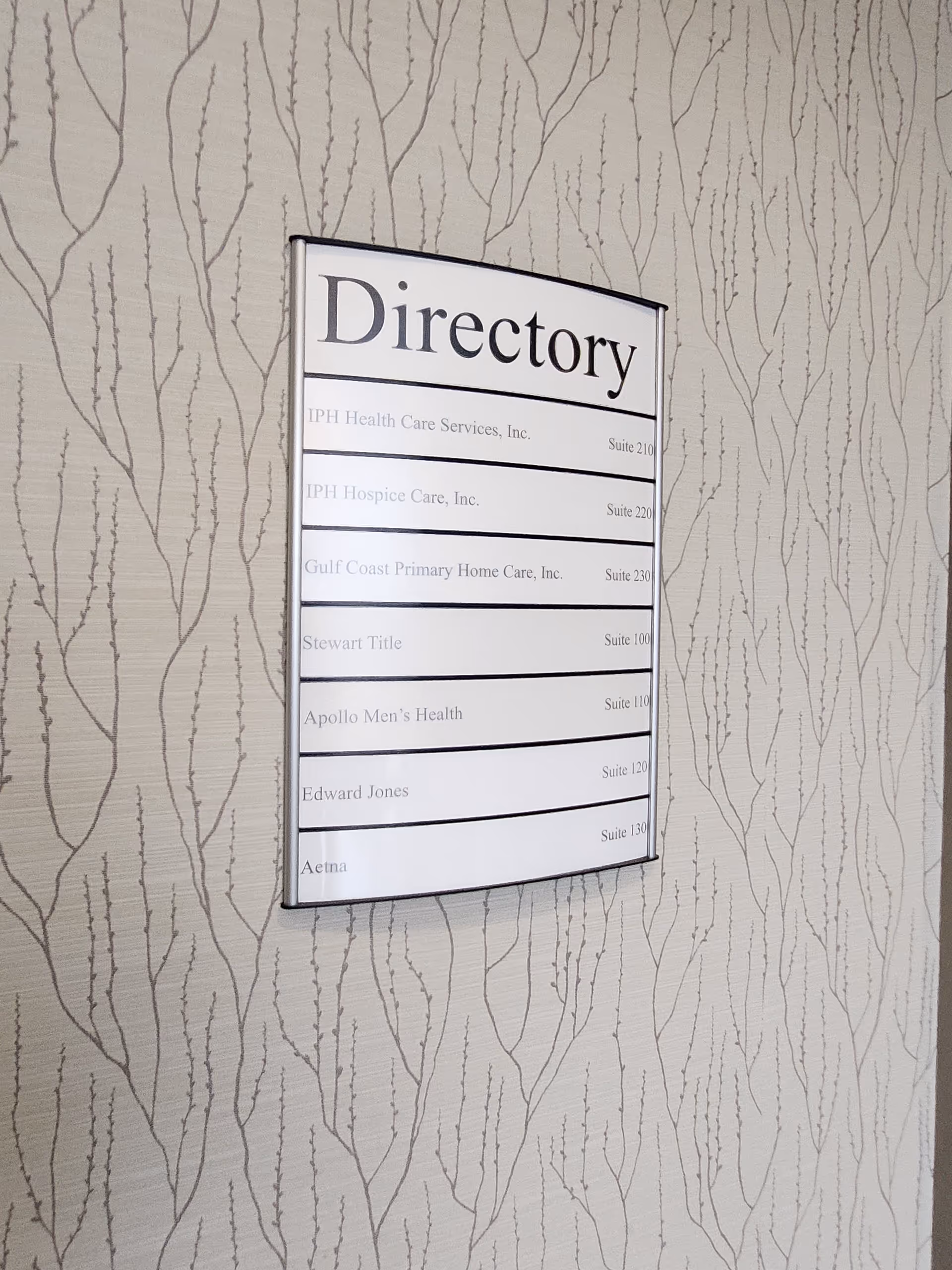 Wall-mounted directory sign on patterned wallpaper in an interior hallway.