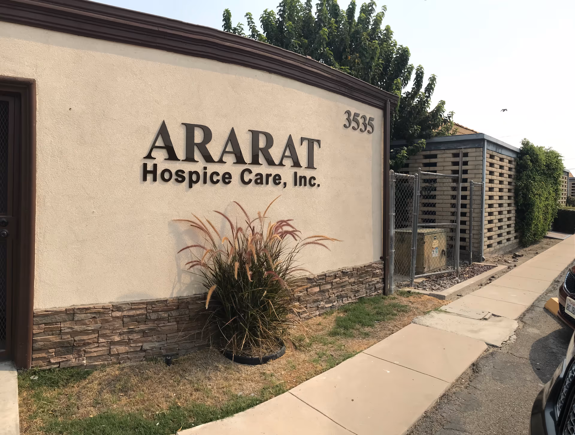 Exterior view of Ararat Hospice Care, Inc. sign on a curved beige wall with plants.