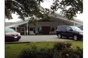 Exterior view of the DeLeon Nursing and Rehab facility with parked cars and a covered entrance.