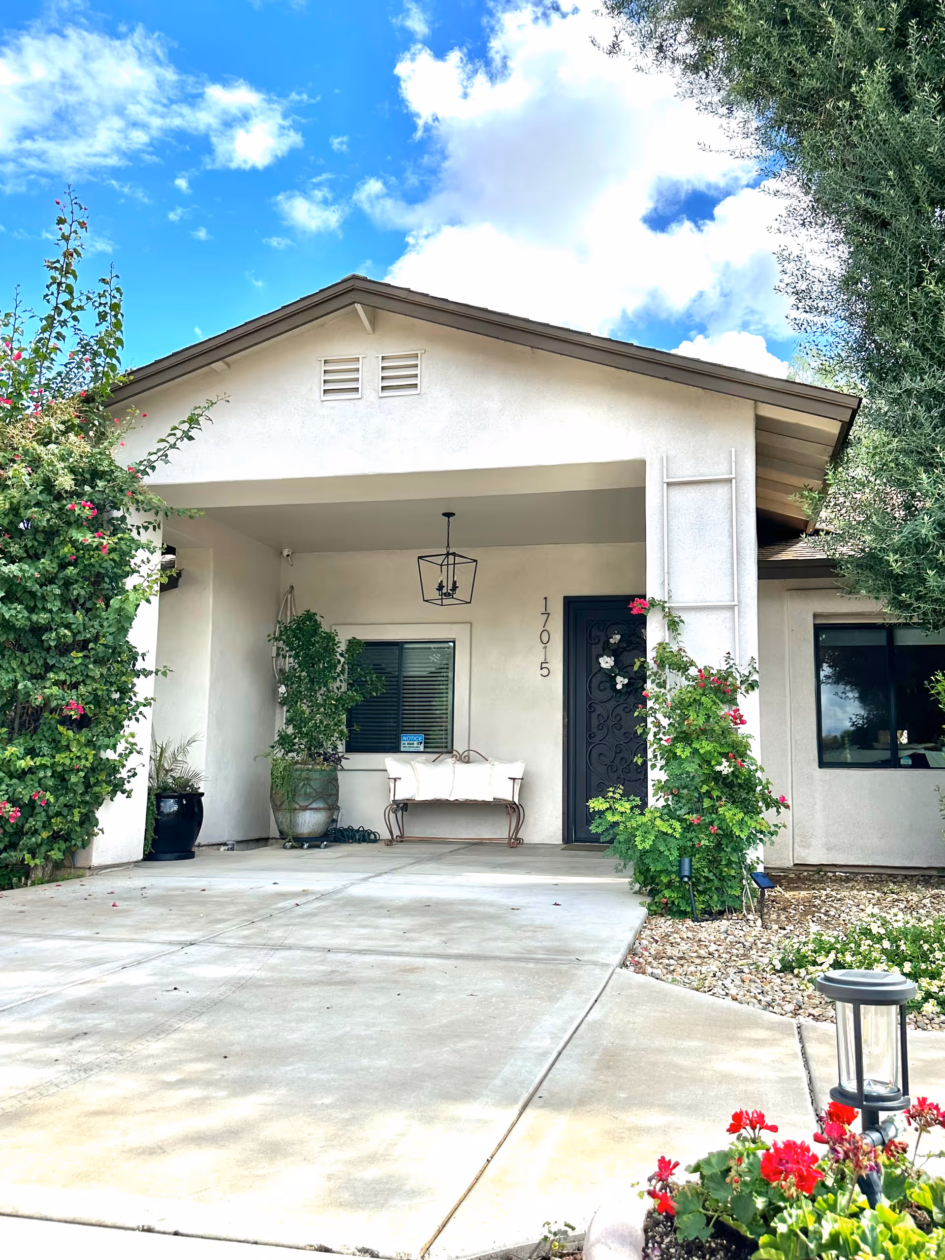 Front exterior of a single-story assisted living home with a porch, bench, and plants.