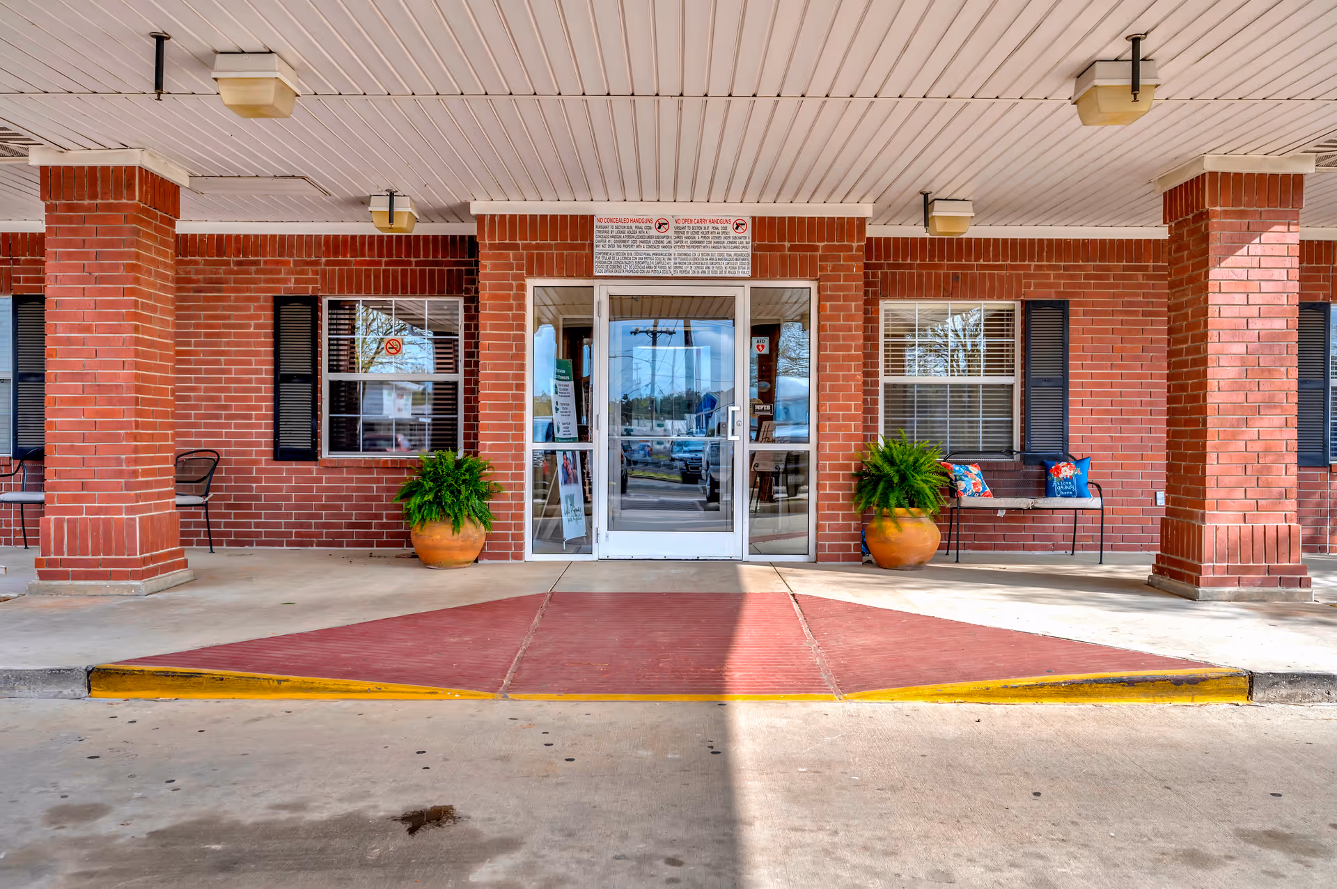 Brick building exterior with glass doors, brick columns, potted plants, and a red entrance ramp.