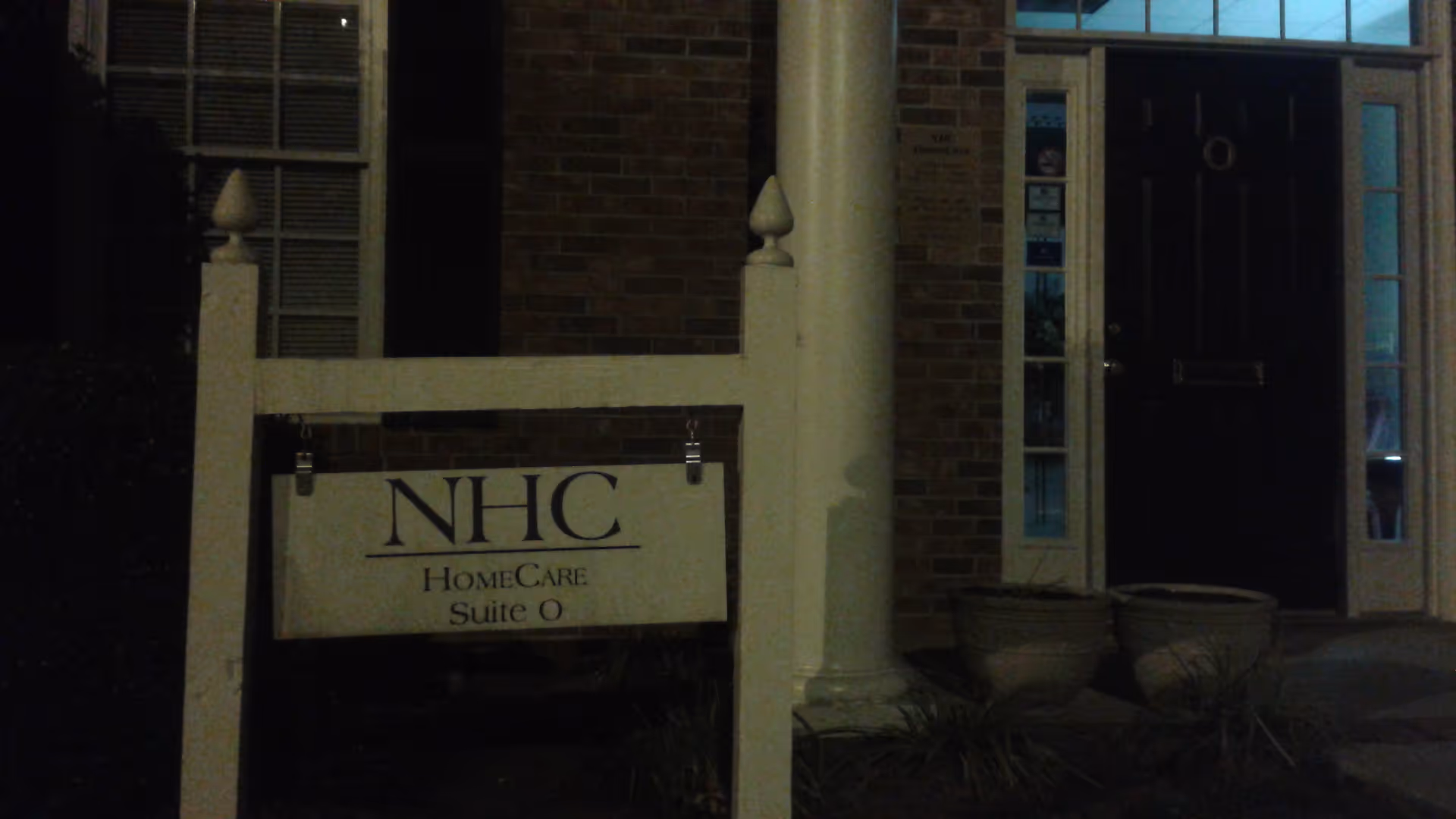 Nighttime exterior of an NHC HomeCare entrance with sign and doorway.