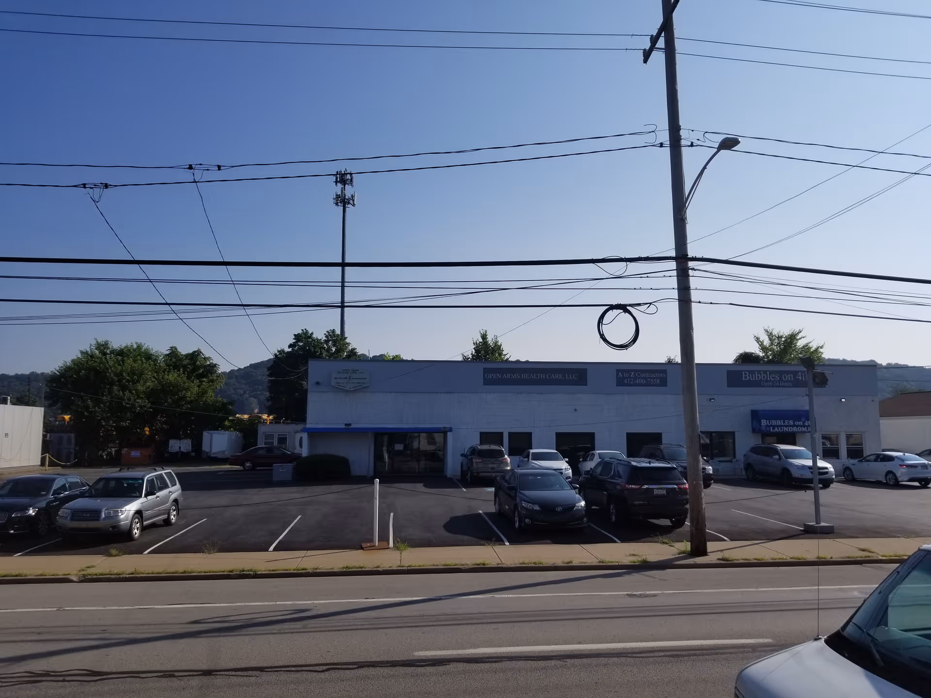 Exterior view of Open Arms Health Care building with parked cars and power lines.