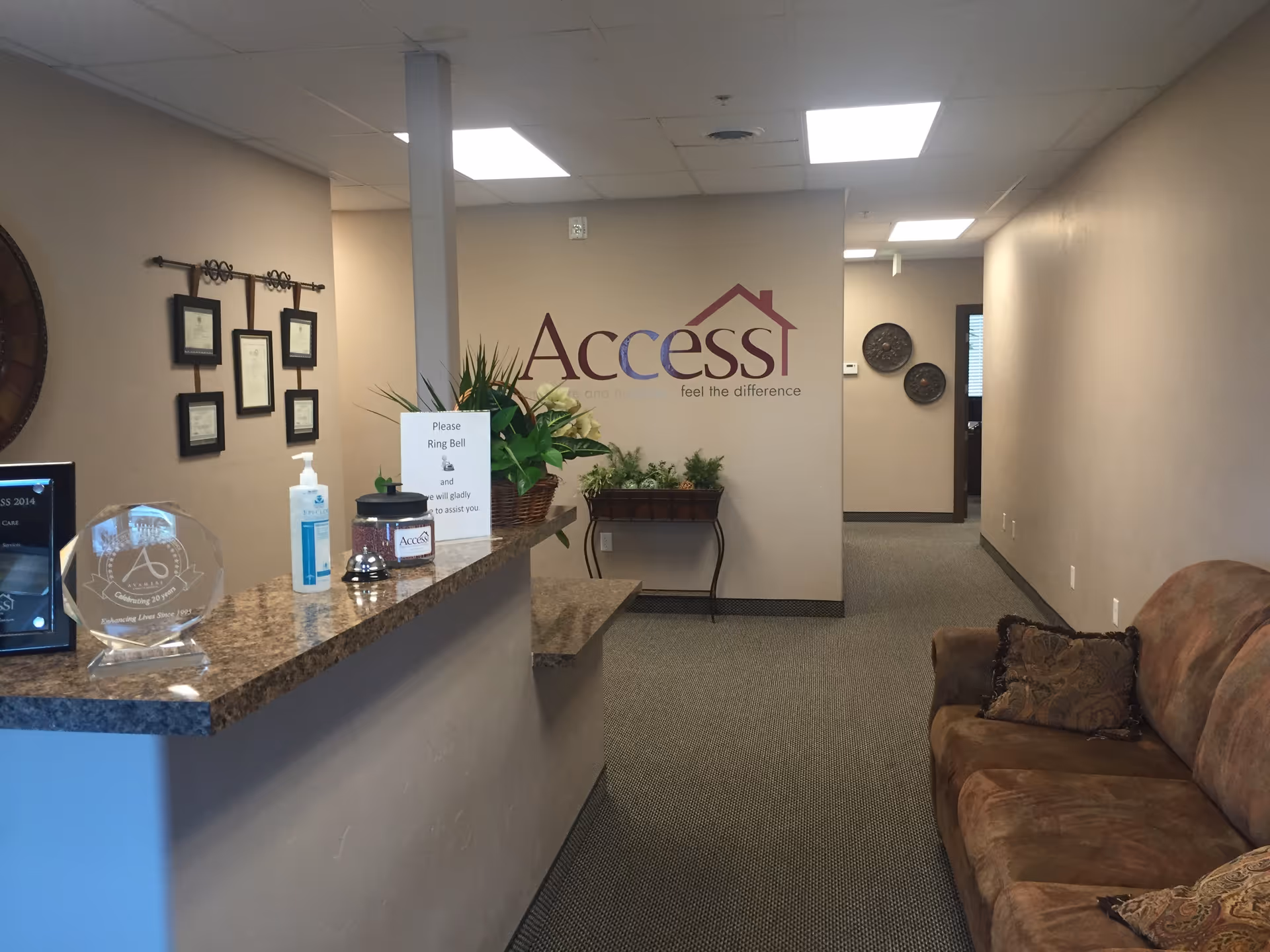 Reception area with granite counter, signage, plants, and a brown sofa in a hallway.