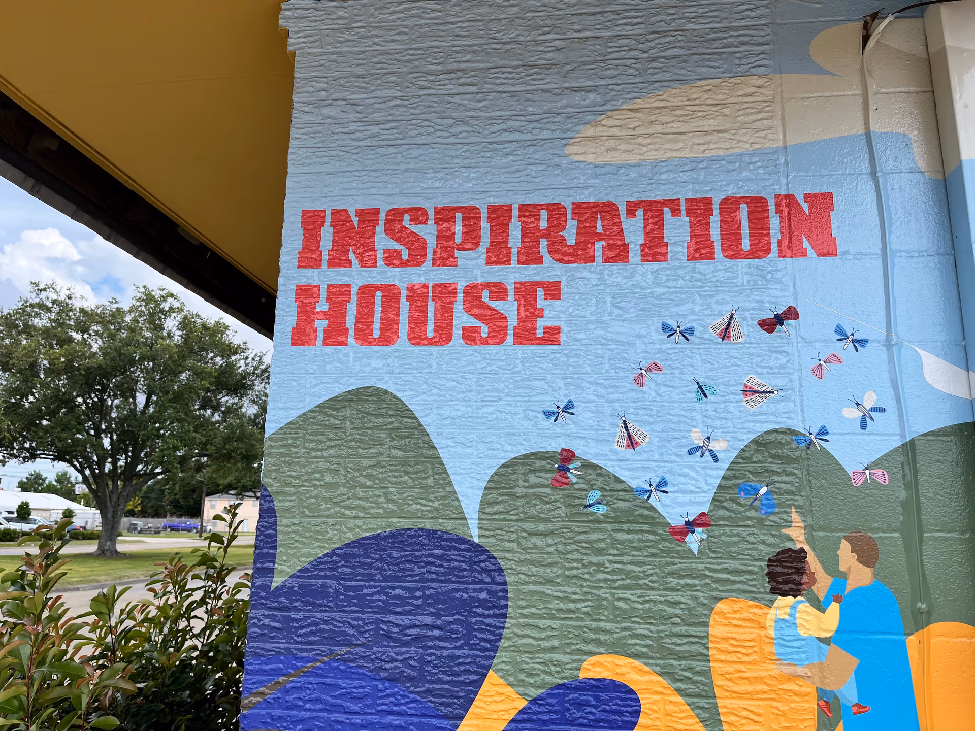 Exterior wall with colorful mural reading Inspiration House, hills, and dragonflies.