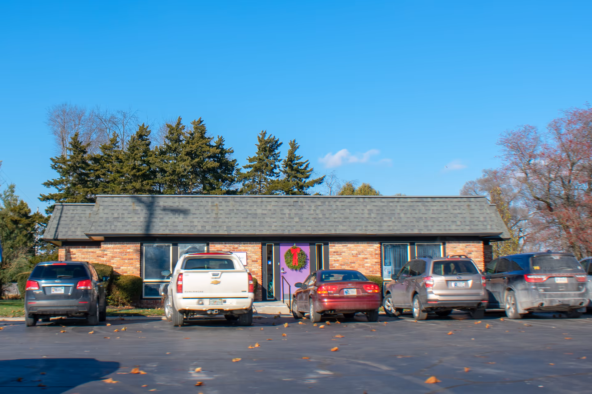 Single-story brick hospice front with parked cars and a wreath by the entrance.