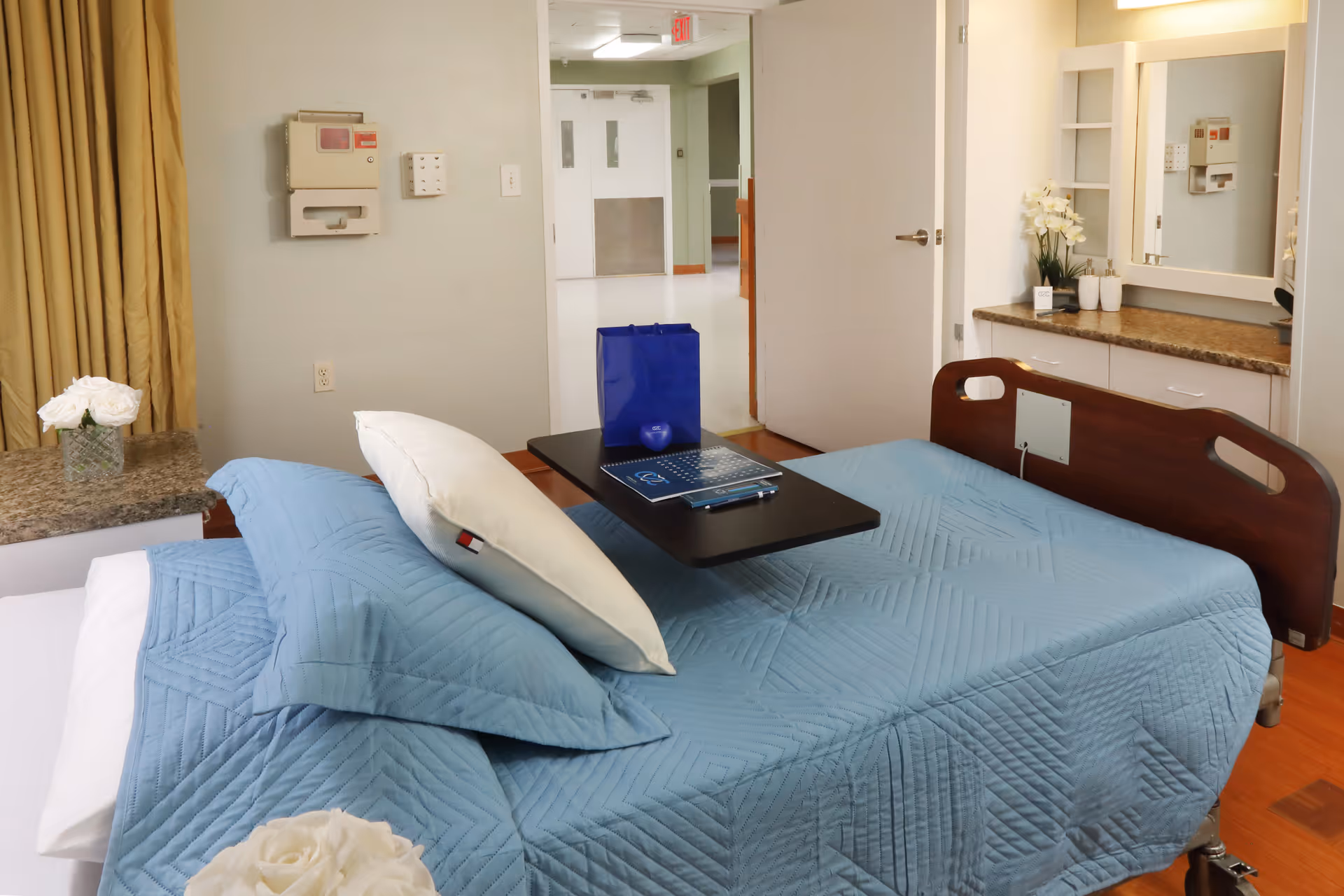 Senior living bedroom with blue quilted bed and vanity area.