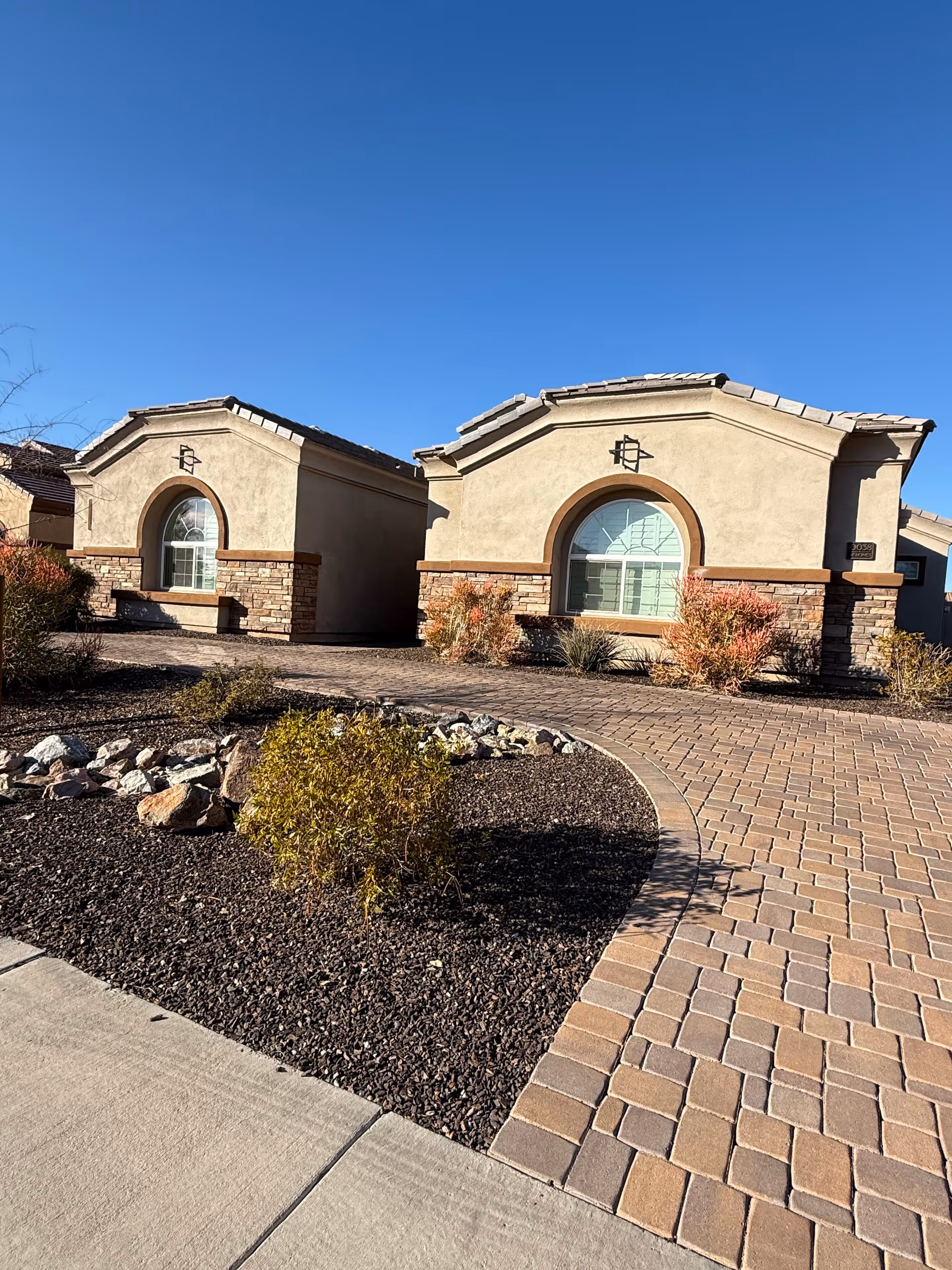 Two beige stucco buildings with arched windows and curved brick walkway.