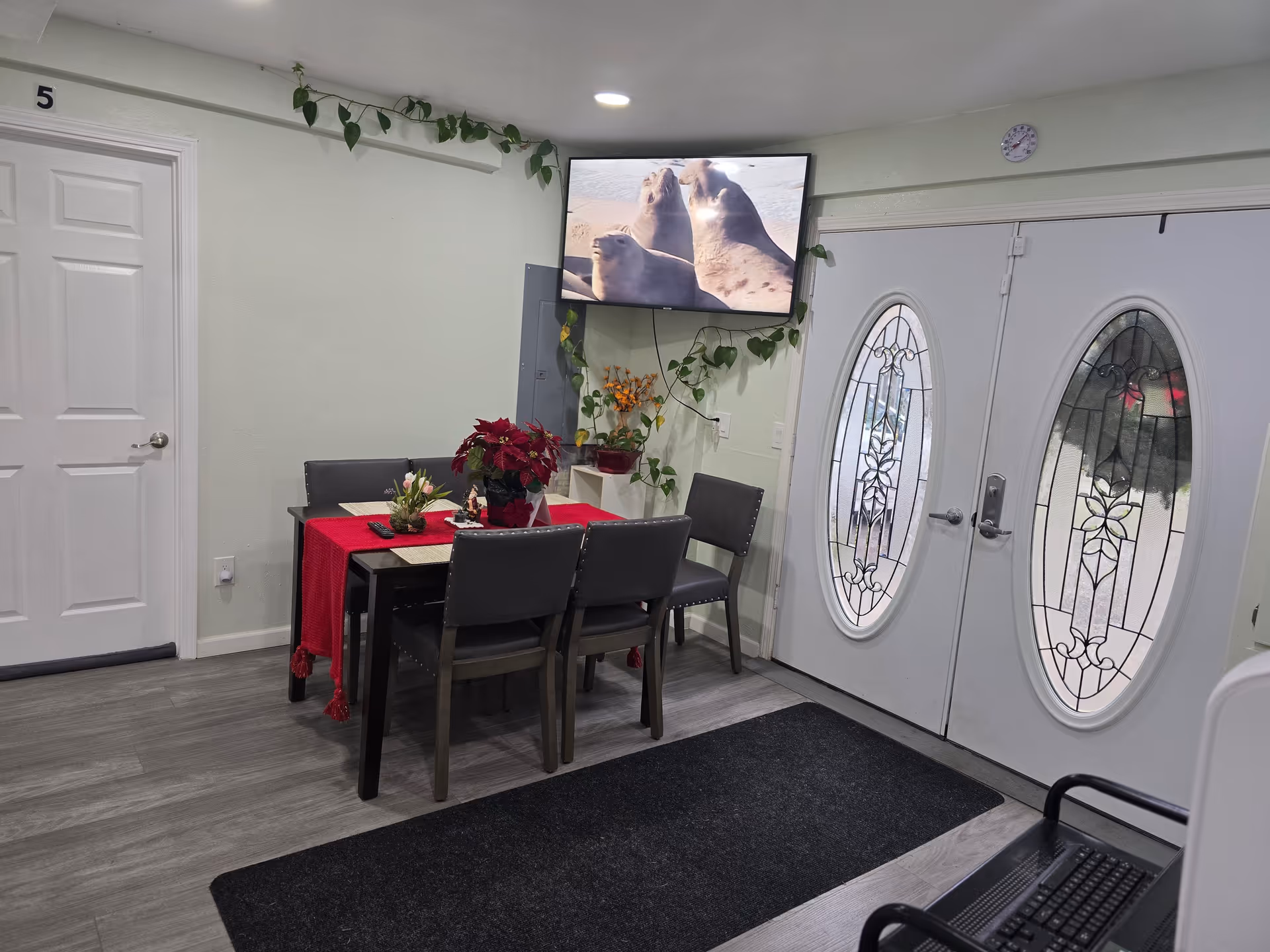 Indoor dining room with a red-tablecloth table, chairs, wall-mounted TV, and decorative doors.
