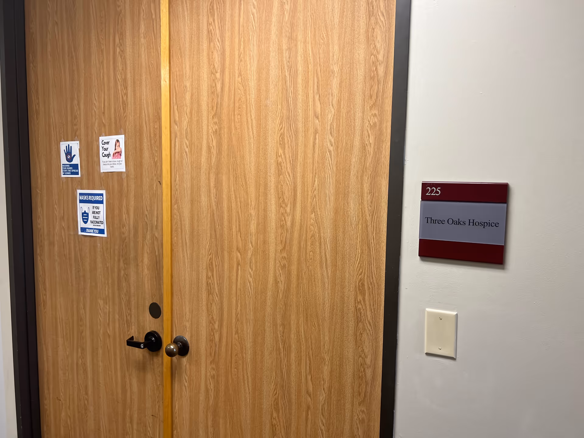 Wooden interior door with safety signs and a wall plaque reading Three Oaks Hospice.
