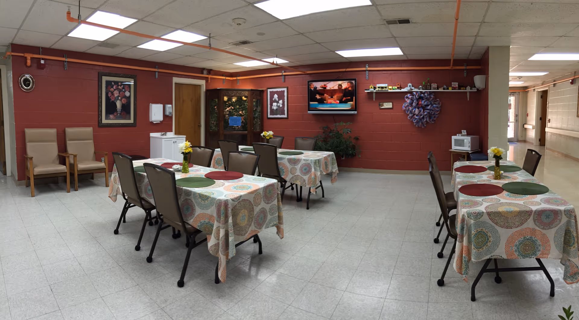 Interior dining room with tables, chairs, and a TV on a red wall.