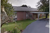 Single-story brick retirement building with a covered entrance, driveway, and grassy lawn.