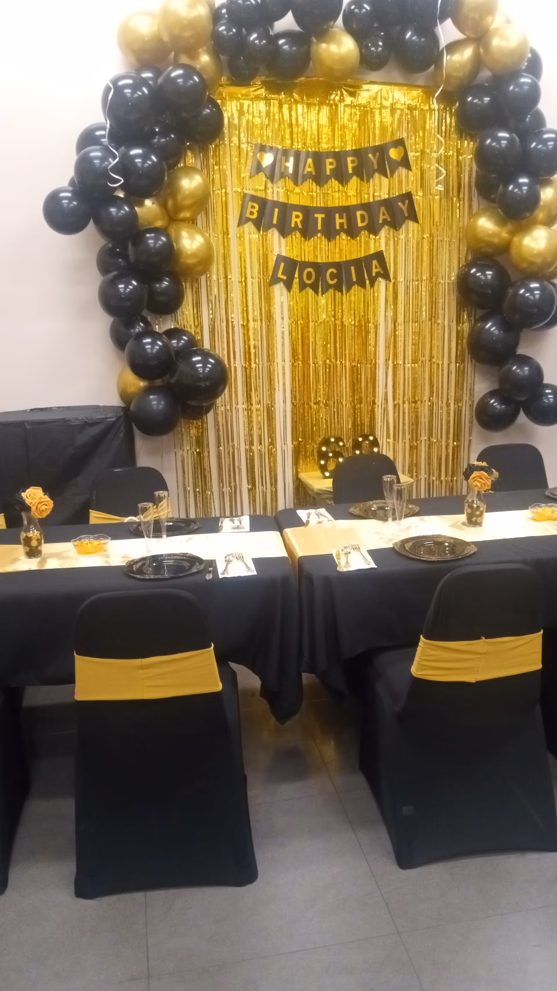 Decorated dining room with black and gold balloons, fringe backdrop, and birthday banner for Lucia