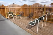Outdoor wooden deck with chairs and a small table enclosed by a wooden fence.