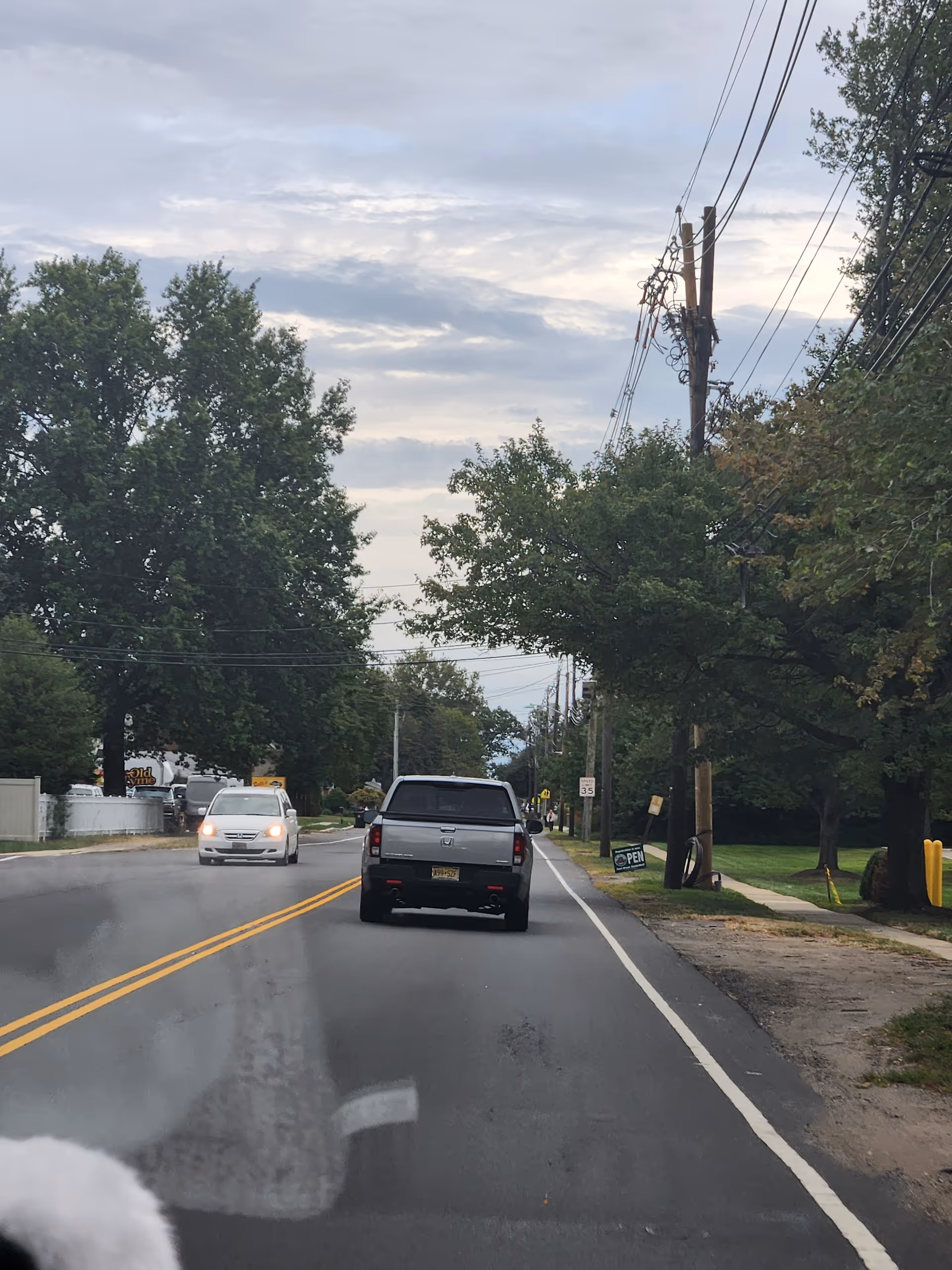 Two-lane street with vehicles, trees, and power lines along a residential sidewalk.