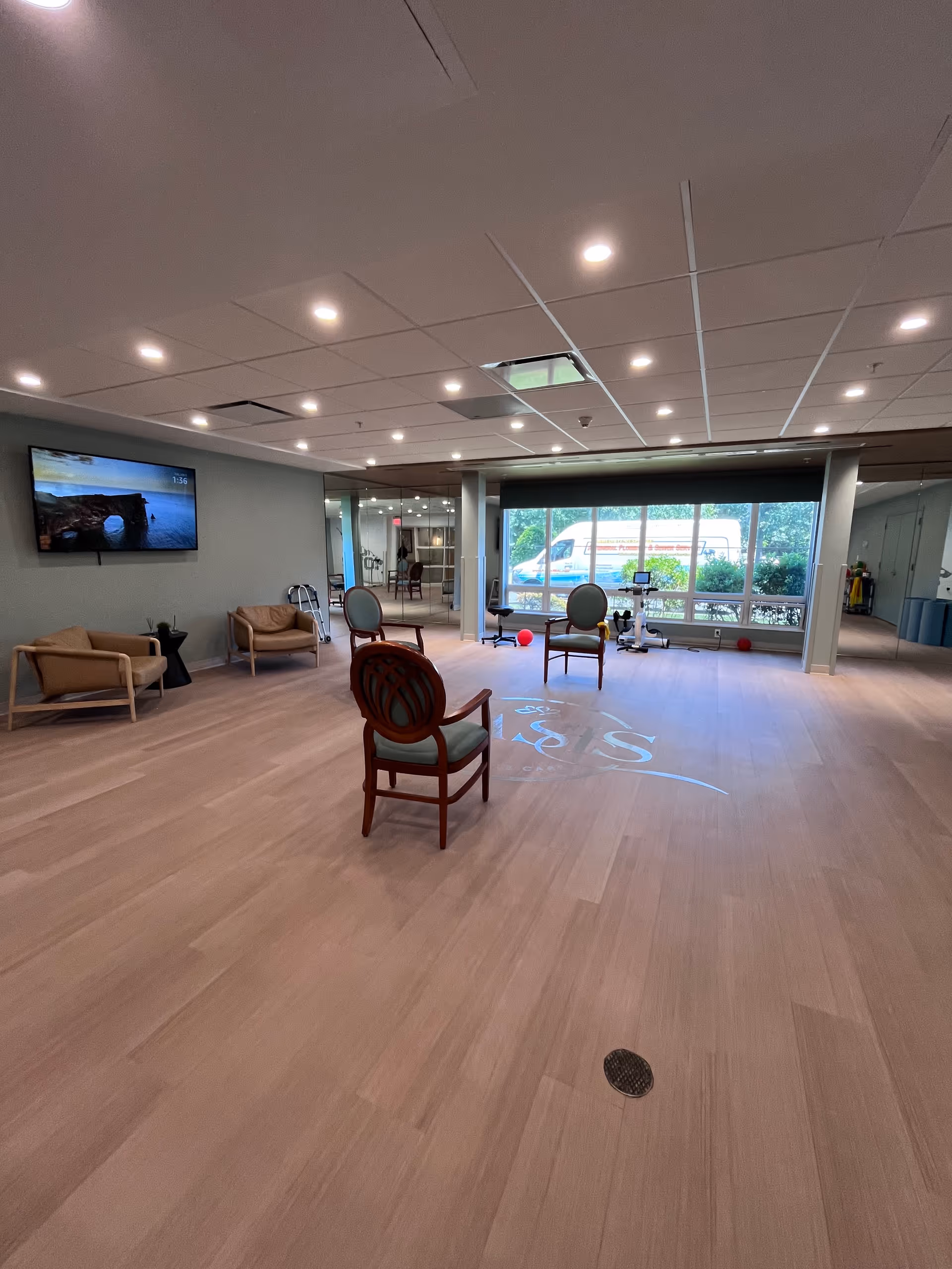 Spacious indoor common area with chairs, TV, and exercise equipment in a senior facility.