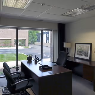 Office workspace with a desk, two chairs, large window, and framed artwork.