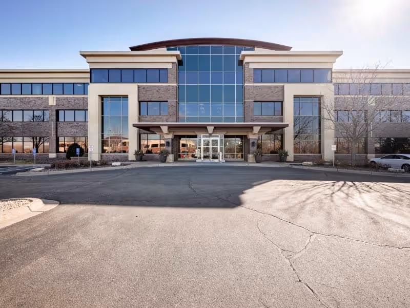 Front exterior of a modern senior living facility with glass entrance and parking lot