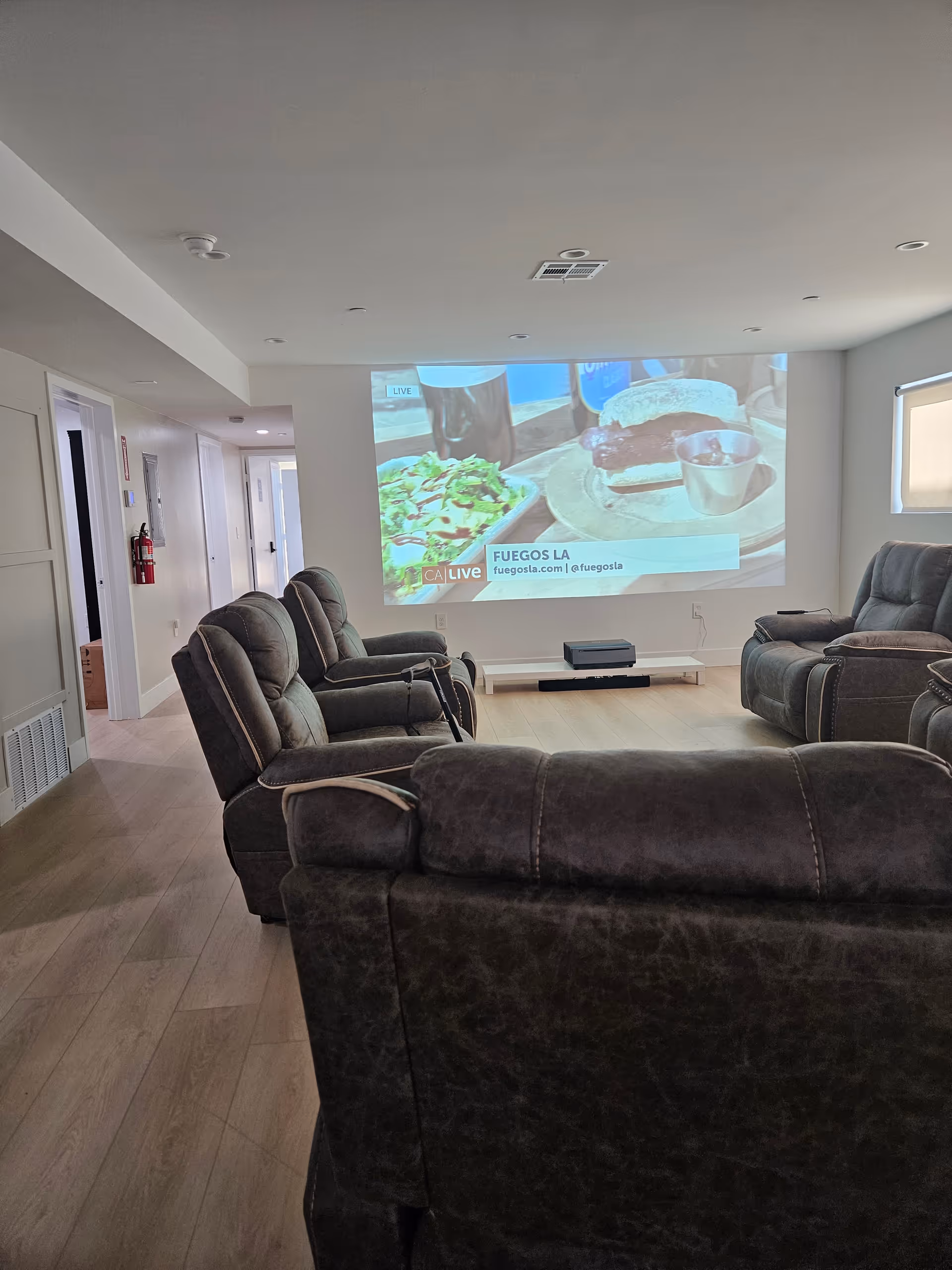 Senior living lounge with projector screen, multiple recliners, and warm wood floors.