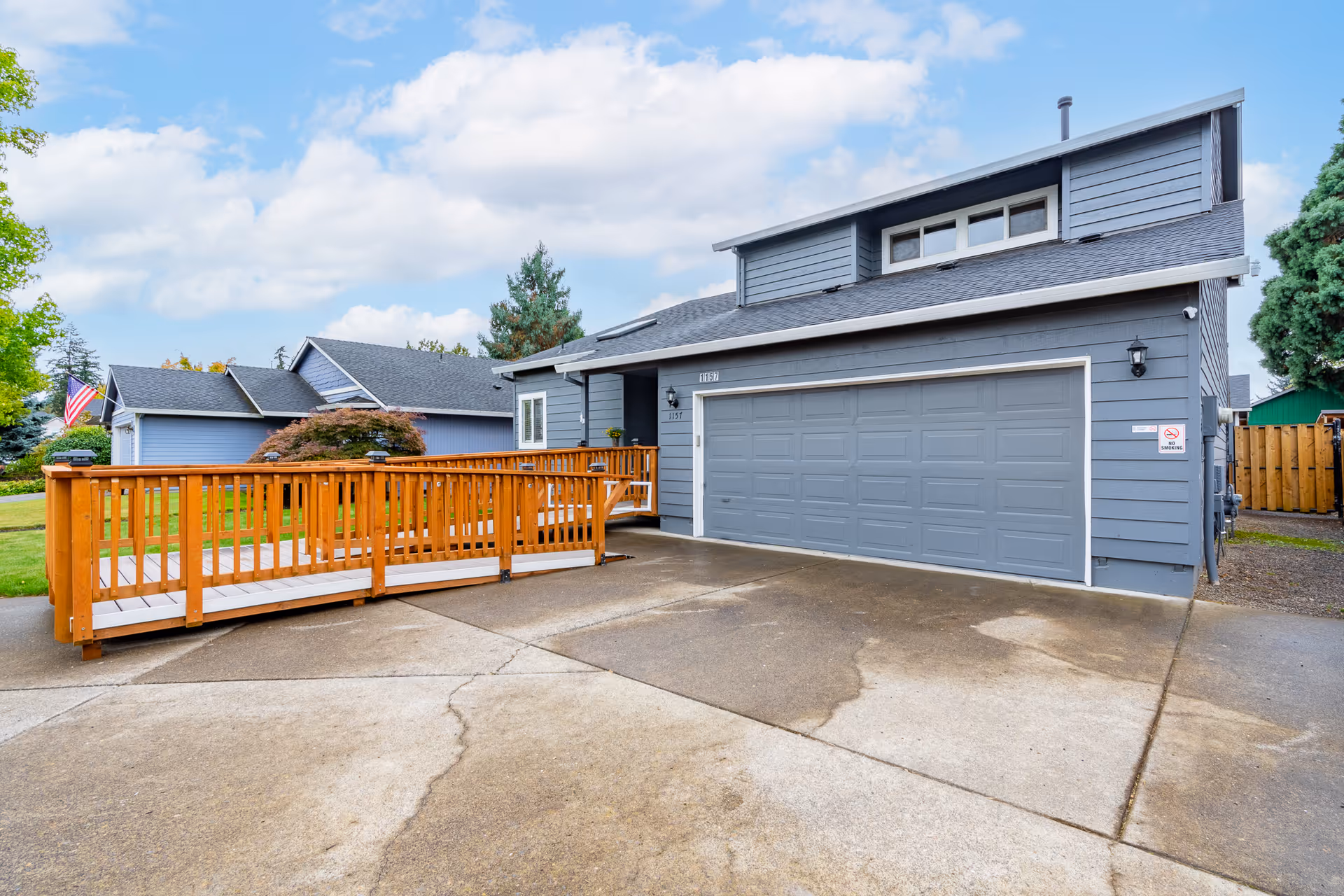 Exterior view of a gray two-story senior living home with a wooden ramp to the entrance.