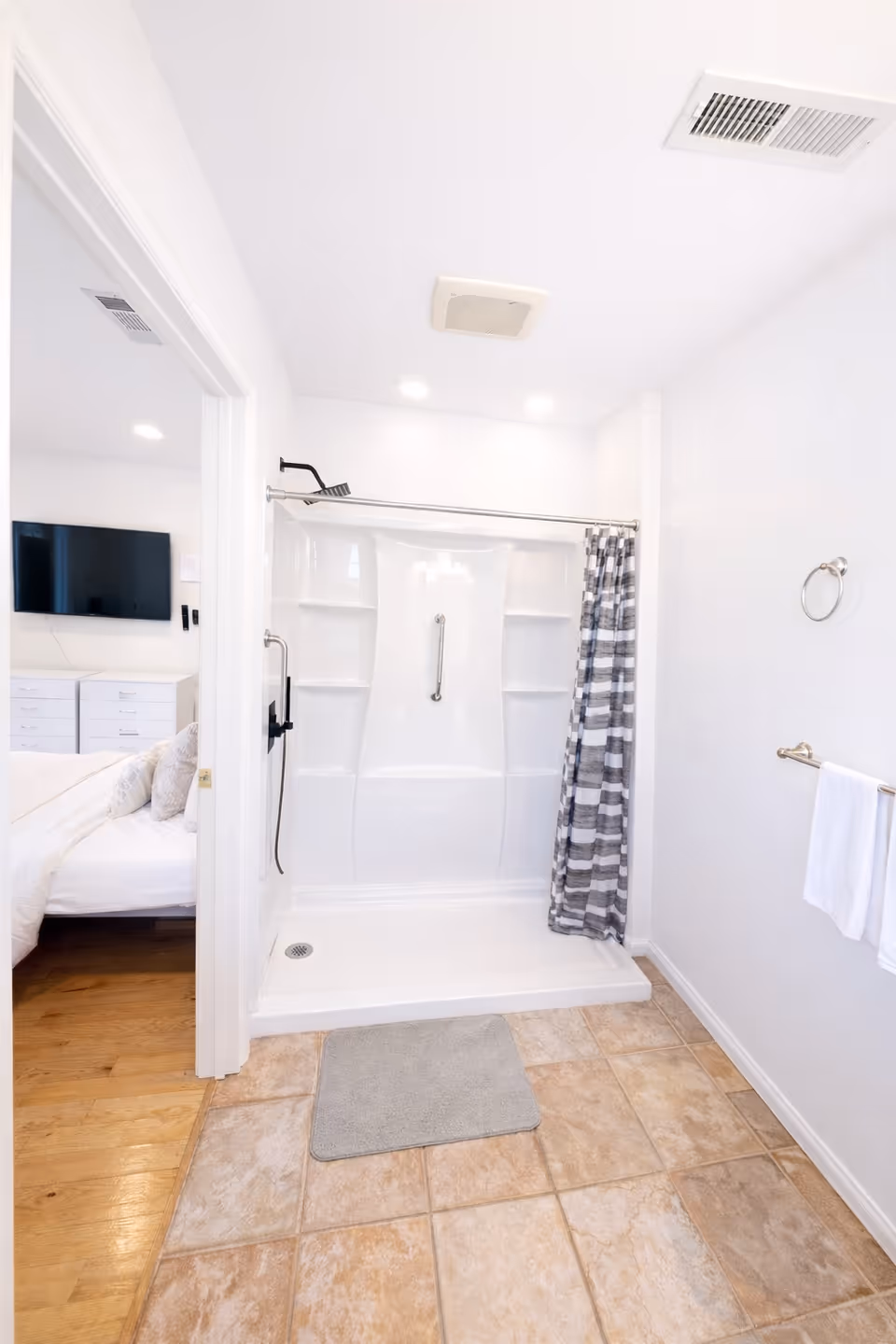 White bathroom with walk-in shower, tiled floor, and doorway to a bedroom.