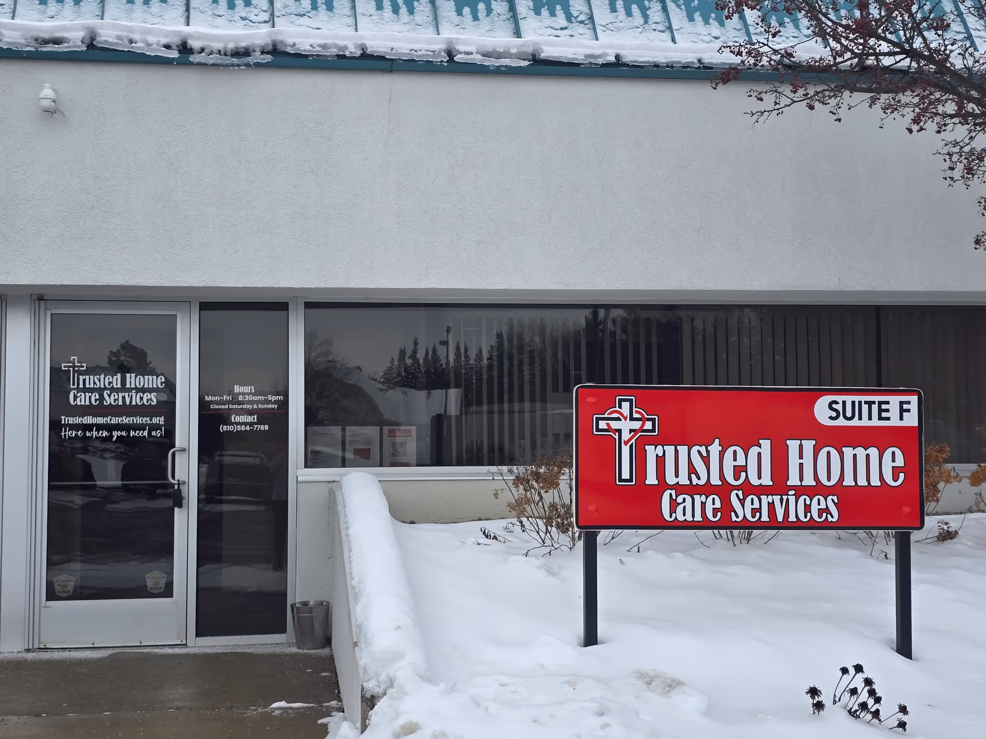 Front exterior of Trusted Home Care Services building with glass entrance and red sign, snowy landscaping.