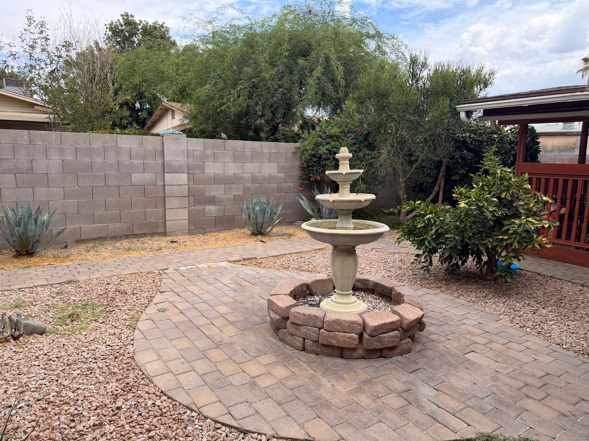 Outdoor courtyard with a stone fountain, brick-paver path, and desert plants.