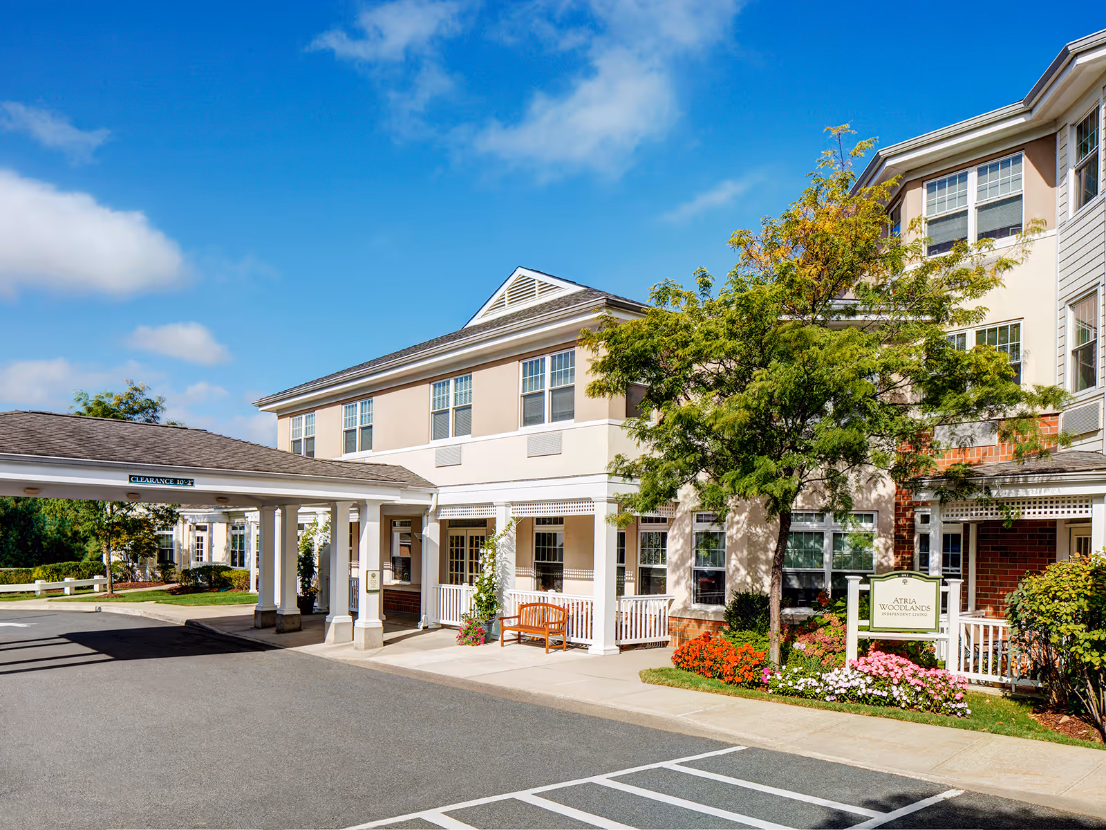 Exterior view of Atria Woodlands senior living facility with a covered entrance and landscaped surroundings.