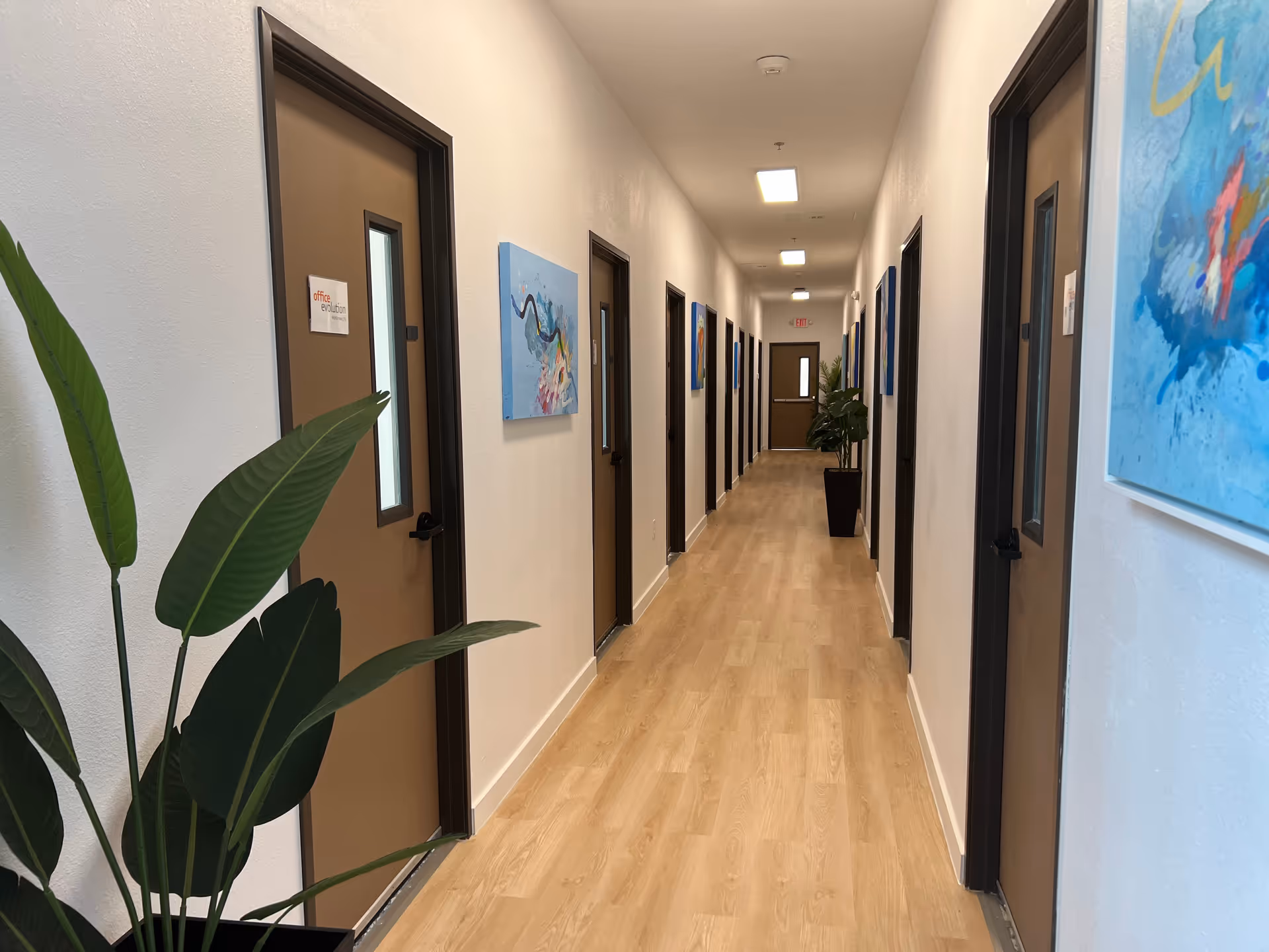 Long, well-lit hallway with closed doors and wall art in a senior living facility.