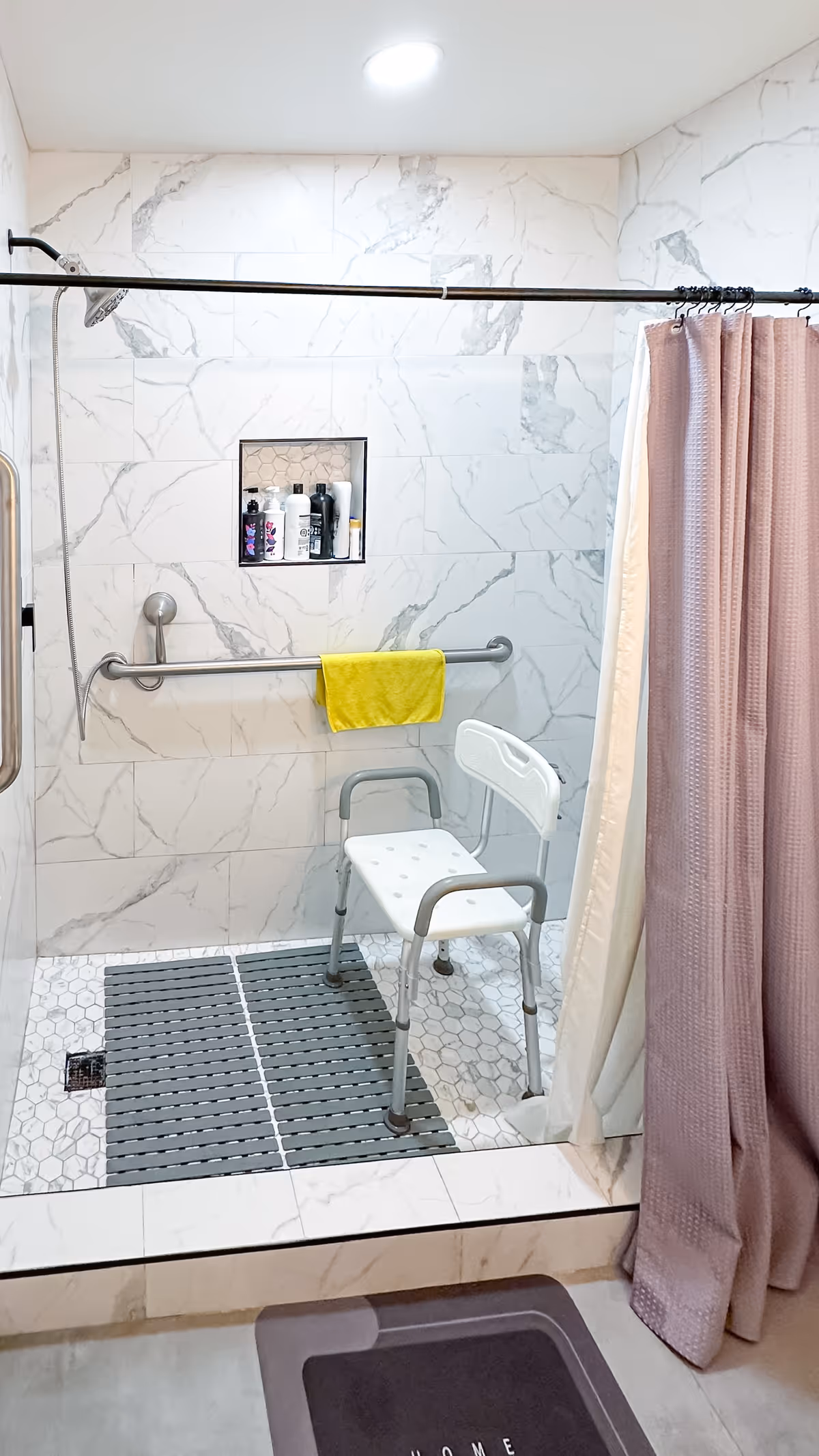 Accessible bathroom with marble-tiled walls, safety grab bars, shower chair, and a sliding shower curtain.