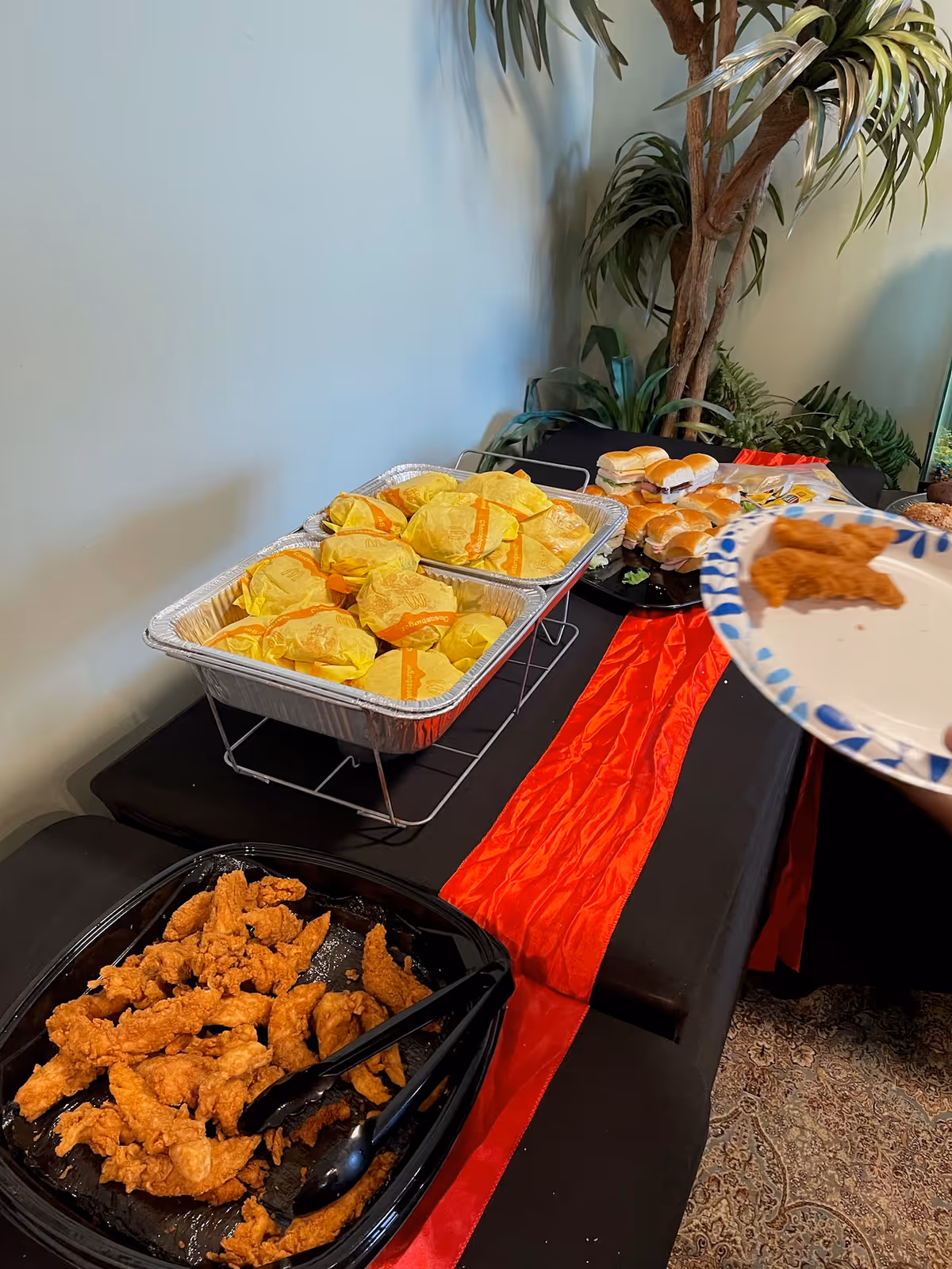 Buffet table with fried chicken, wrapped sandwiches, and plates in a dining area