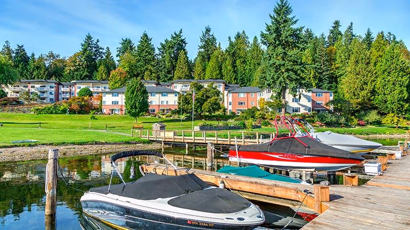 Boats docked along a wooden pier with green lawns and residential buildings beyond.