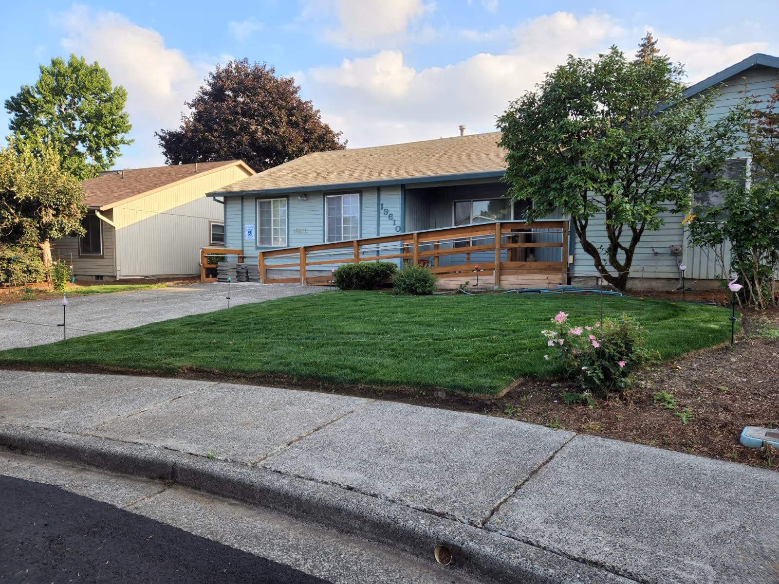 Blue, single-story facility with a wooden ramp, green lawn, trees, and sidewalk.