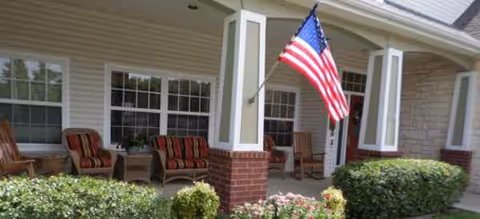 Front porch of Brookdale Western Hills featuring seating, columns, and an American flag.