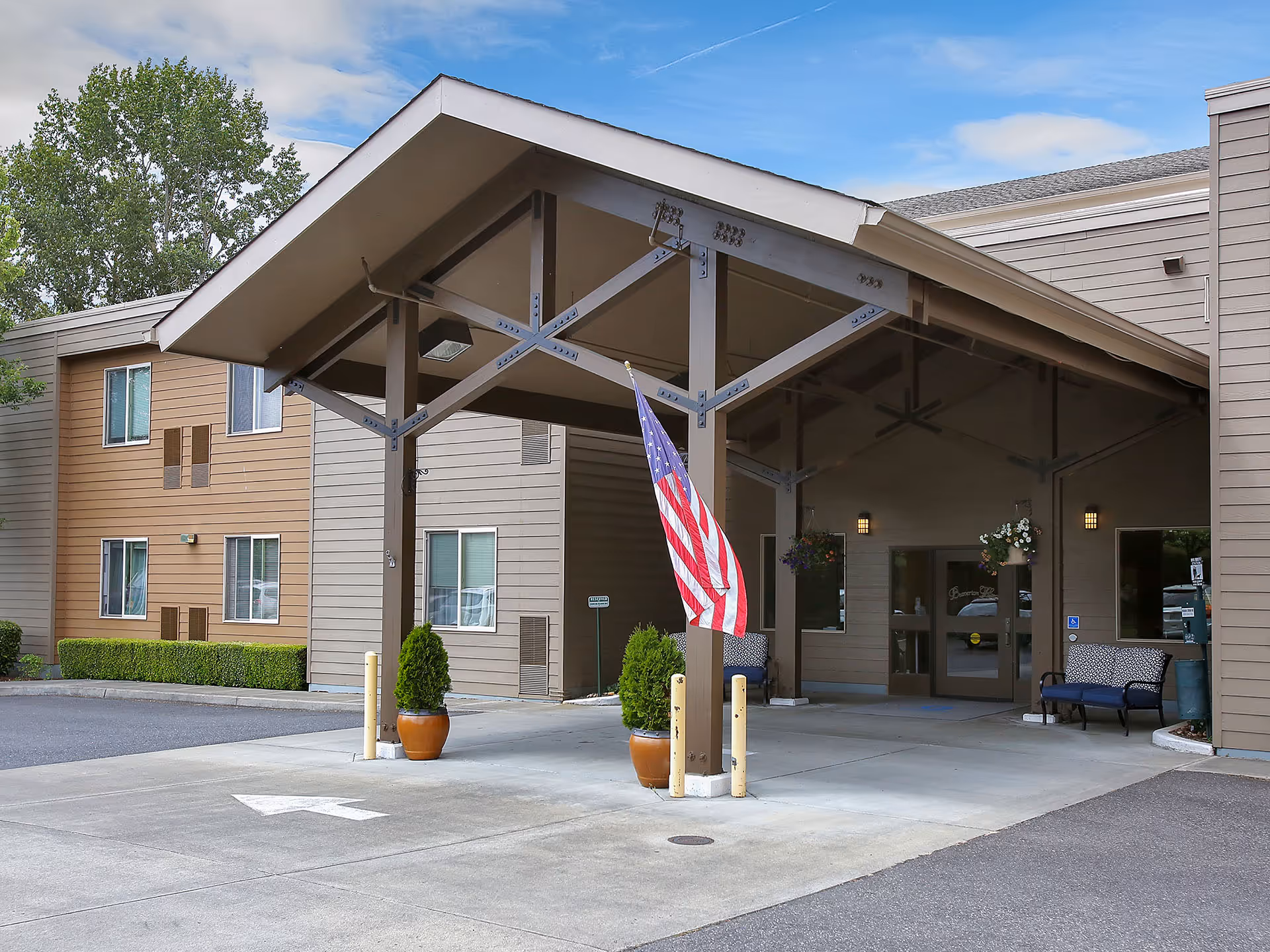 Exterior view of Prestige Senior Living Beaverton Hills entrance with a covered drop-off and flag.