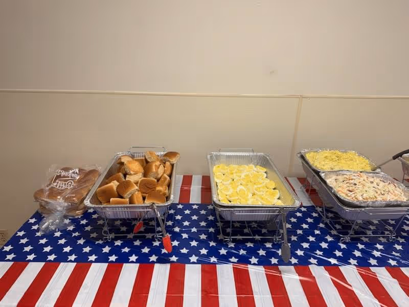 Buffet spread of buns, lemon slices, and casseroles on a star-spangled tablecloth indoors.