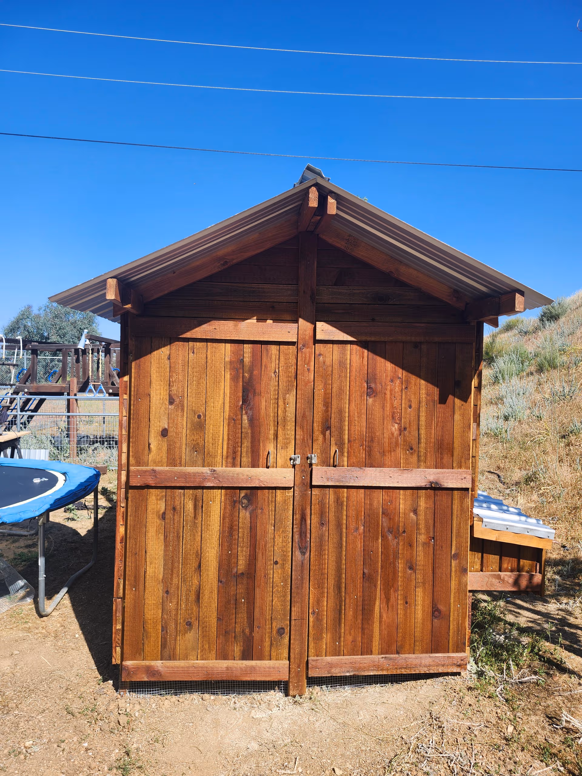 Front view of a wooden shed with double doors outdoors beside a trampoline.
