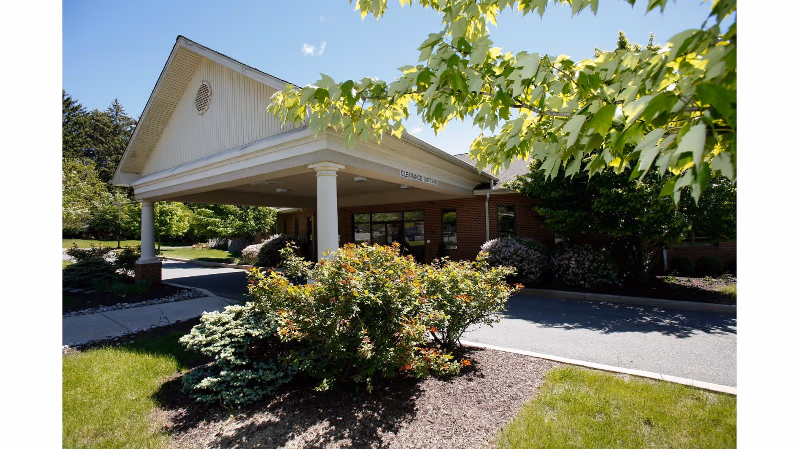 Front view of a brick senior living facility entrance with a covered portico and landscaping.