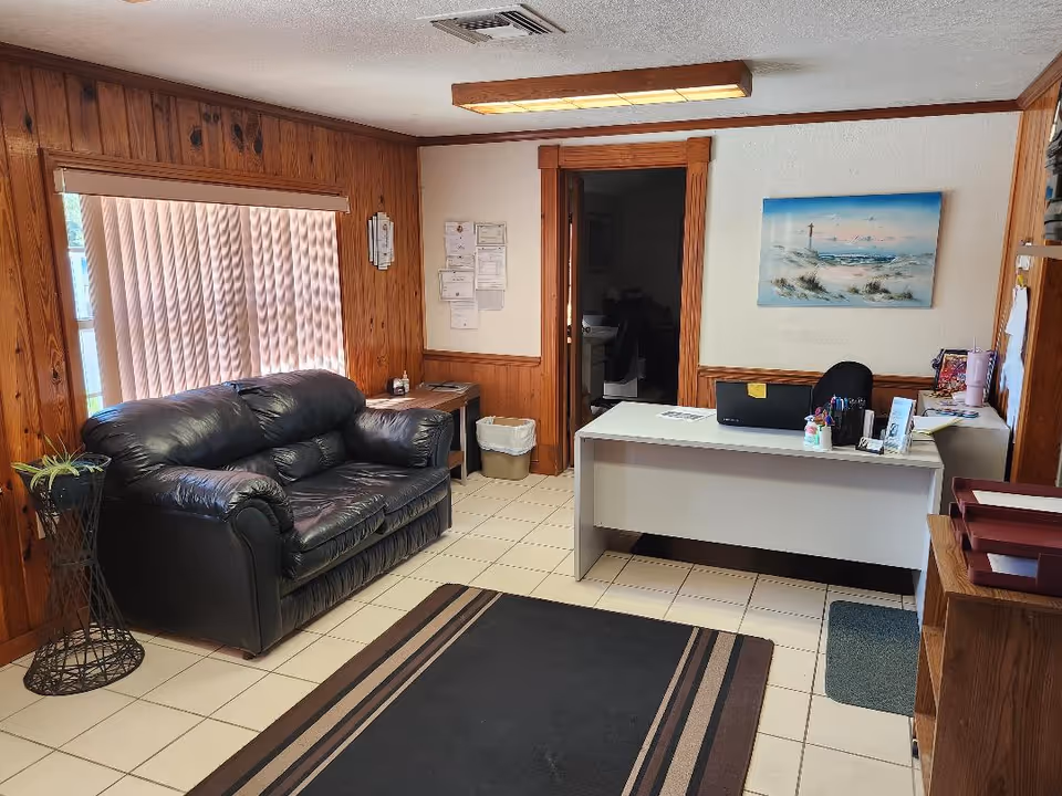 Reception desk with computer, leather sofa, and wood-paneled walls in a senior living lobby.