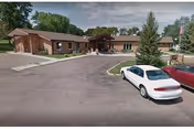Front view of Select Senior Living II exterior with driveway and parked cars.